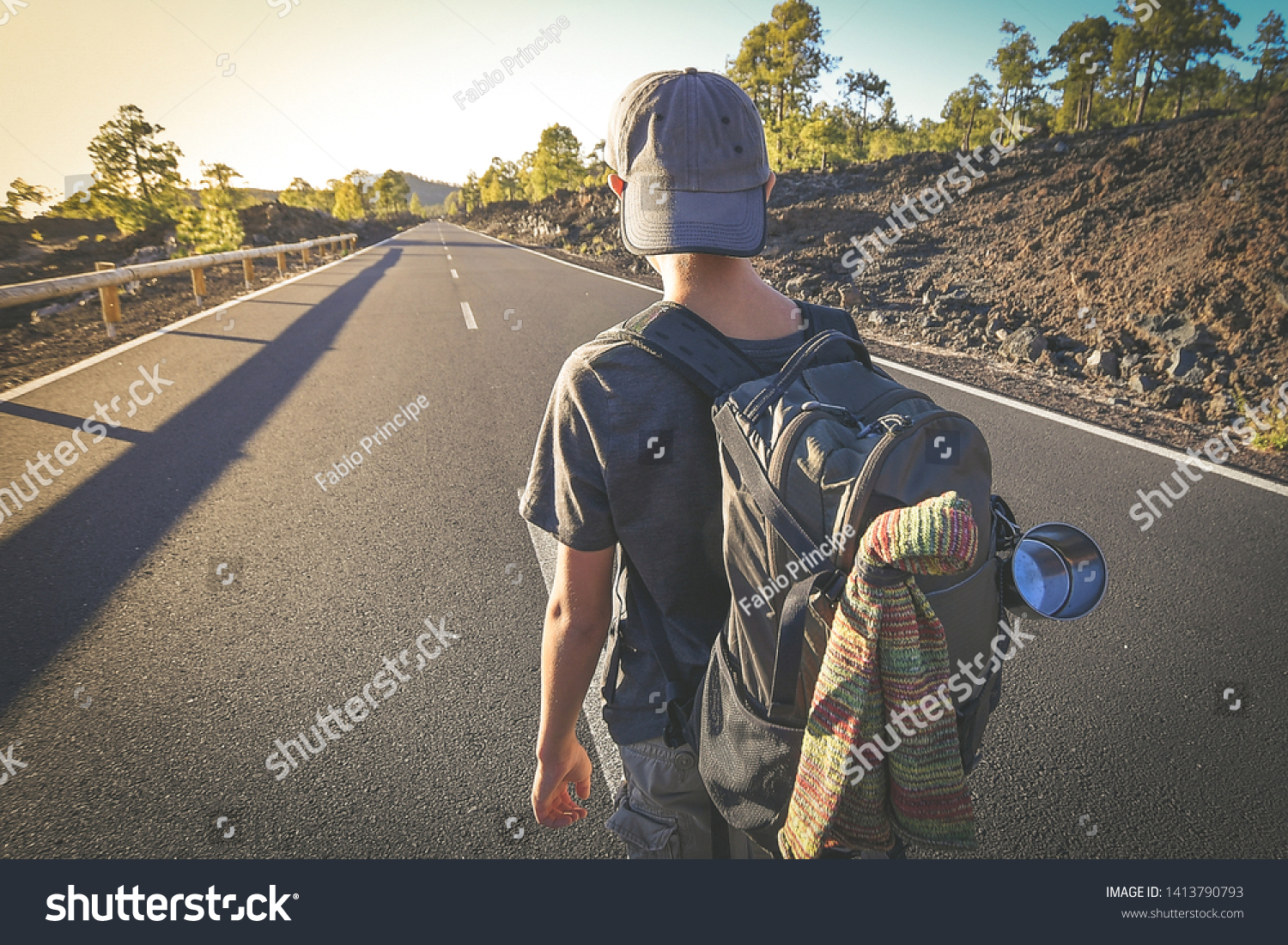 Back view of a young boy walks alone in the middle of the street. Teen with backpack leaving after the end of school Man walking to a new travel adventure. Positive, brave, and adventurous concept. #1413790793