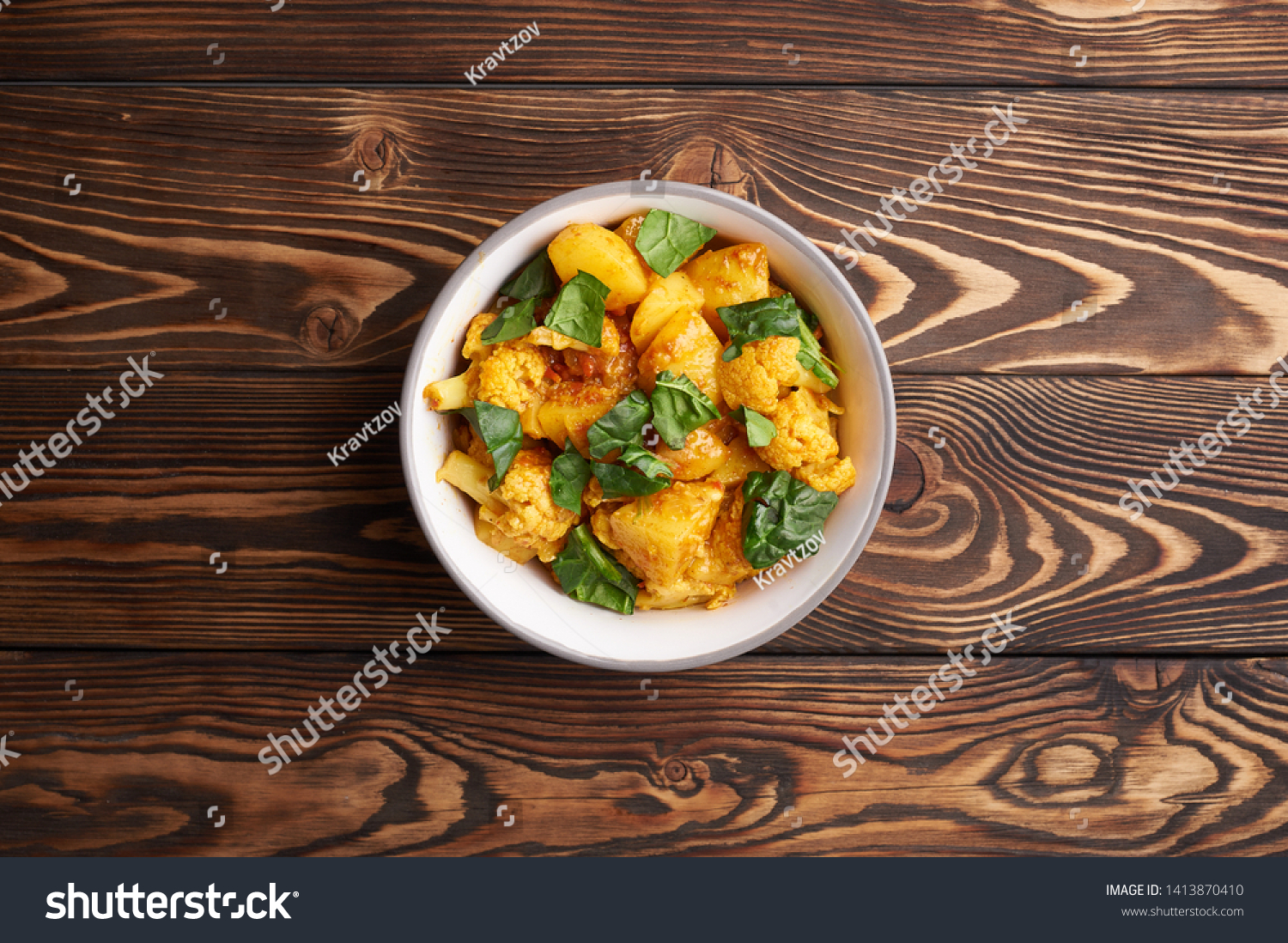 aloo gobi. Indian cuisine vegetarian curry cooked with cauliflower, potato, ginger, garlic and spices - cumin, coriander, chili and garam masala. brown woden table top #1413870410