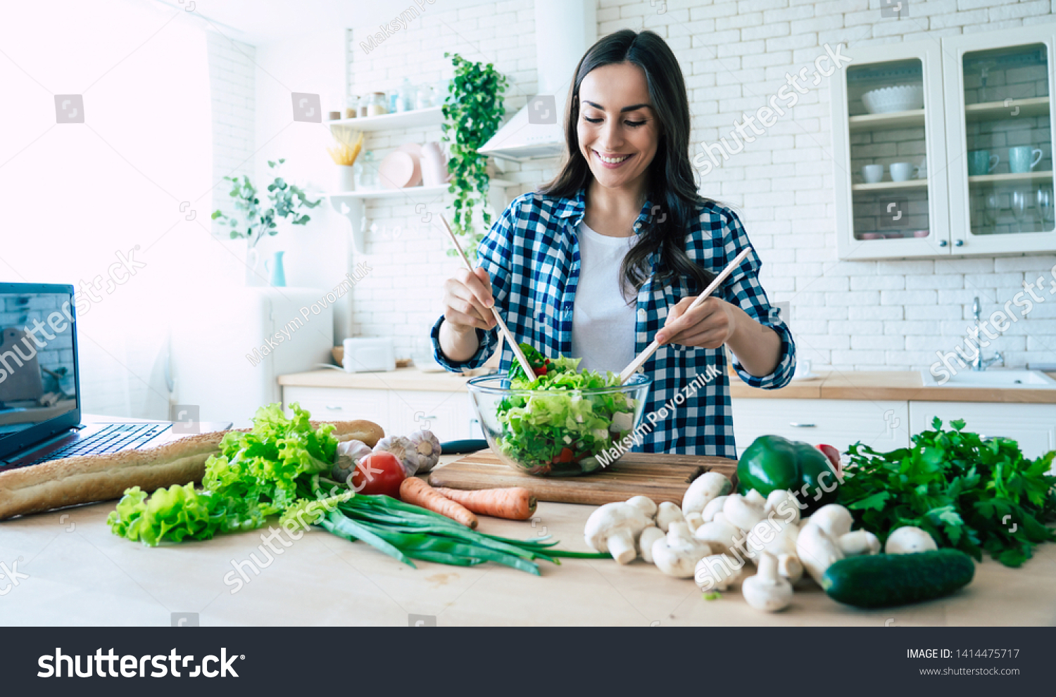 Beautiful young woman is preparing vegetable salad in the kitchen. Healthy Food. Vegan Salad. Diet. Dieting Concept. Healthy Lifestyle. Cooking At Home. Prepare Food. Cutting ingredients on table #1414475717