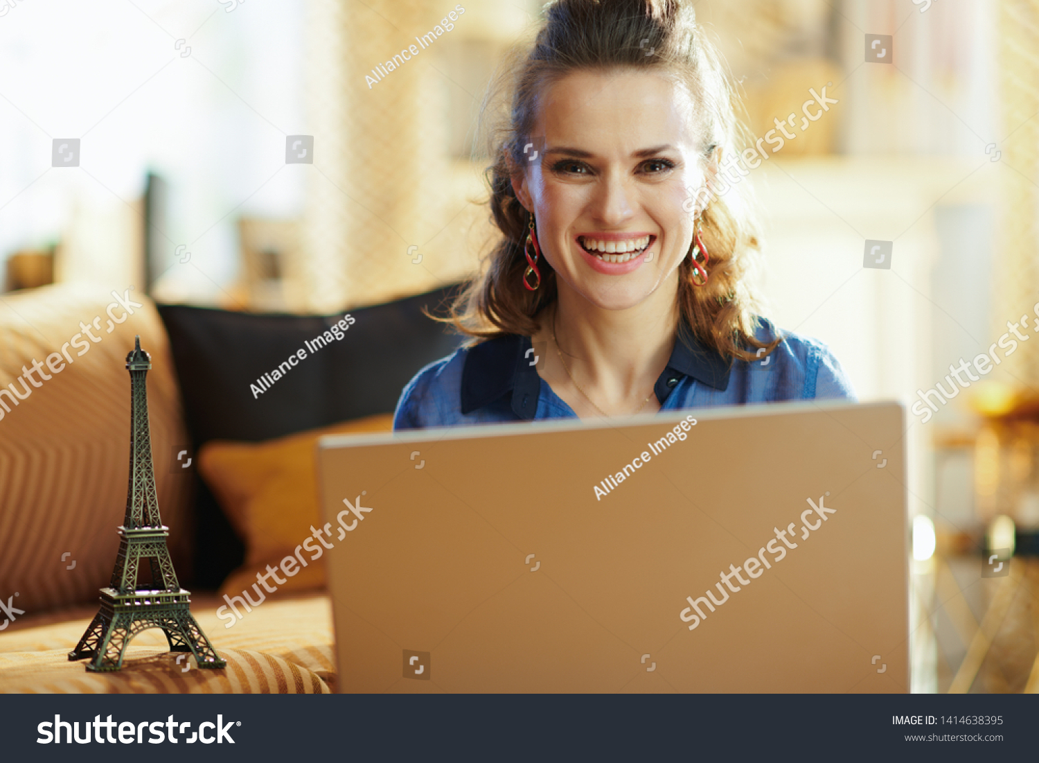 happy modern woman with a souvenir of the eiffel tower using laptop at modern home in sunny summer day. A fake website is made for illustrative purposes. #1414638395