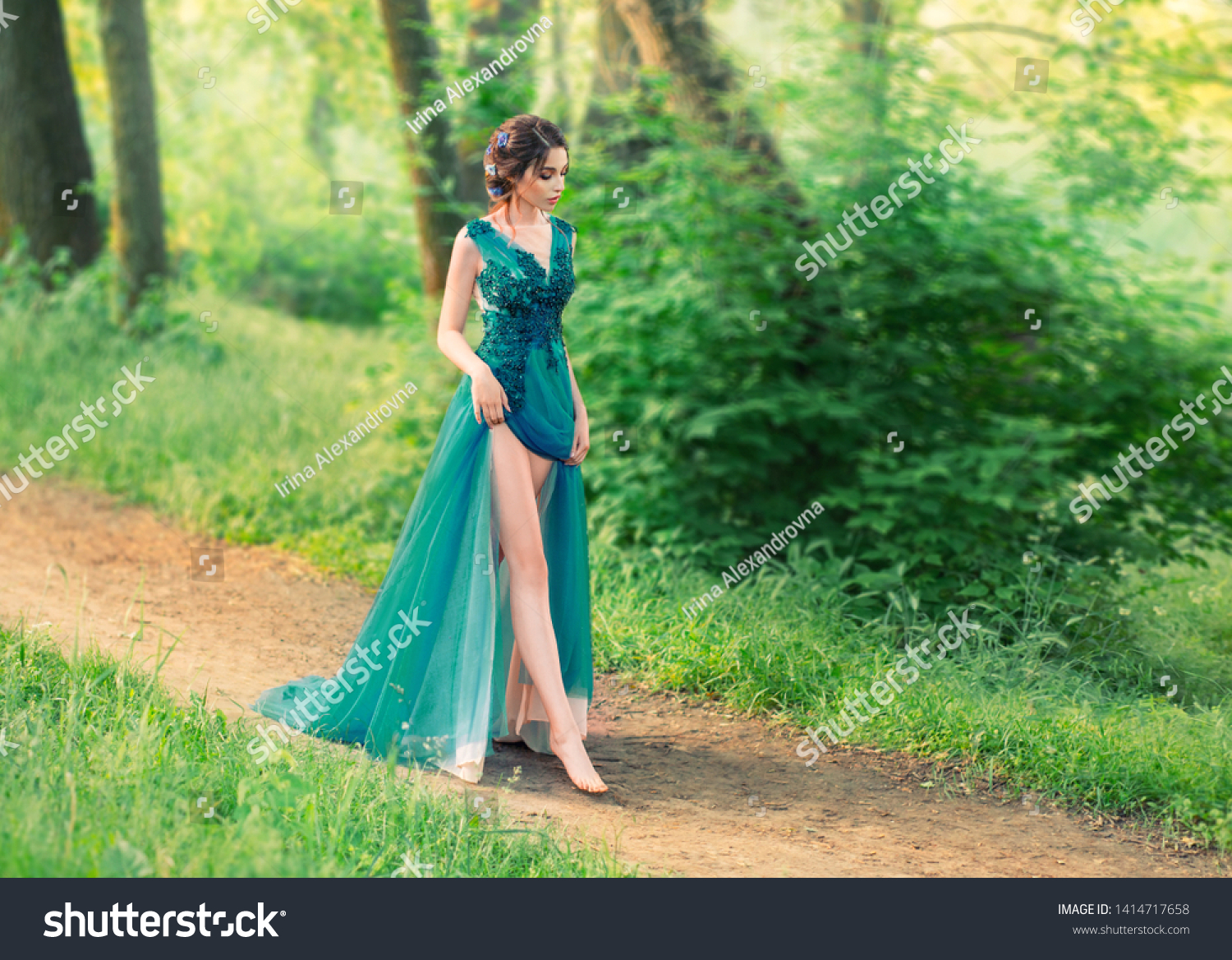 charming gentle angel descended from sky and cautiously walks along forest path. cute princess in long elegant elegant expensive dress with dark braided hair decorated with flowers, sexy bare legs #1414717658