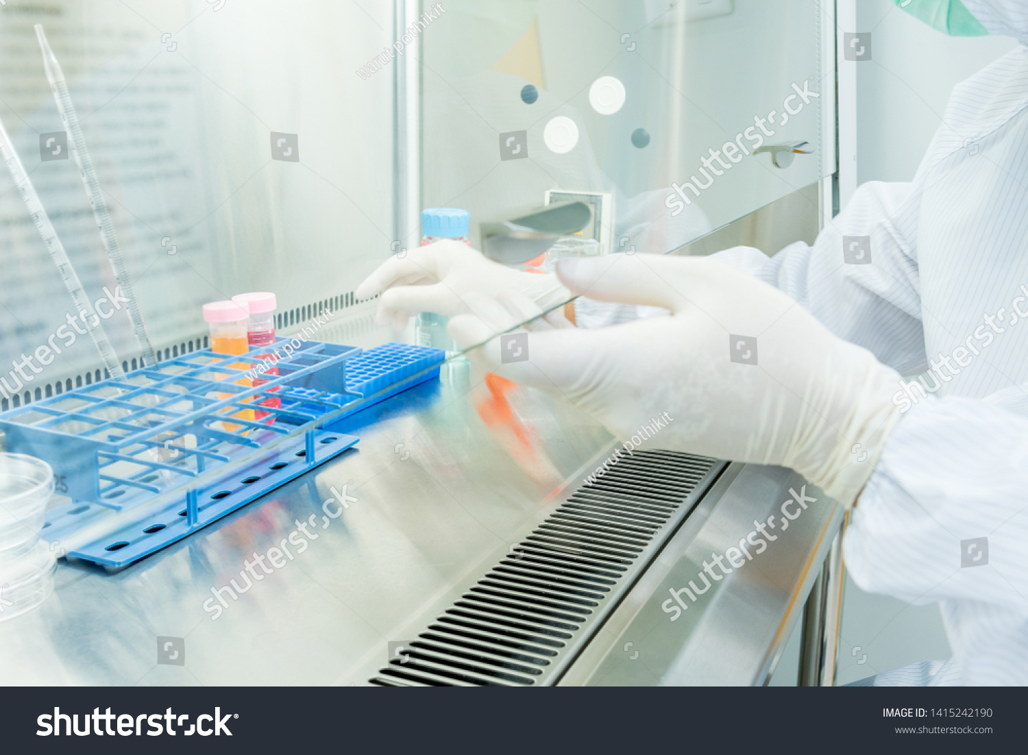 A scientist in sterile coverall gown preparing growth medium and reagent for cell cuture assay in biological safety cabinet (BSC). Doing molecular experiment in cleanroom facility. #1415242190