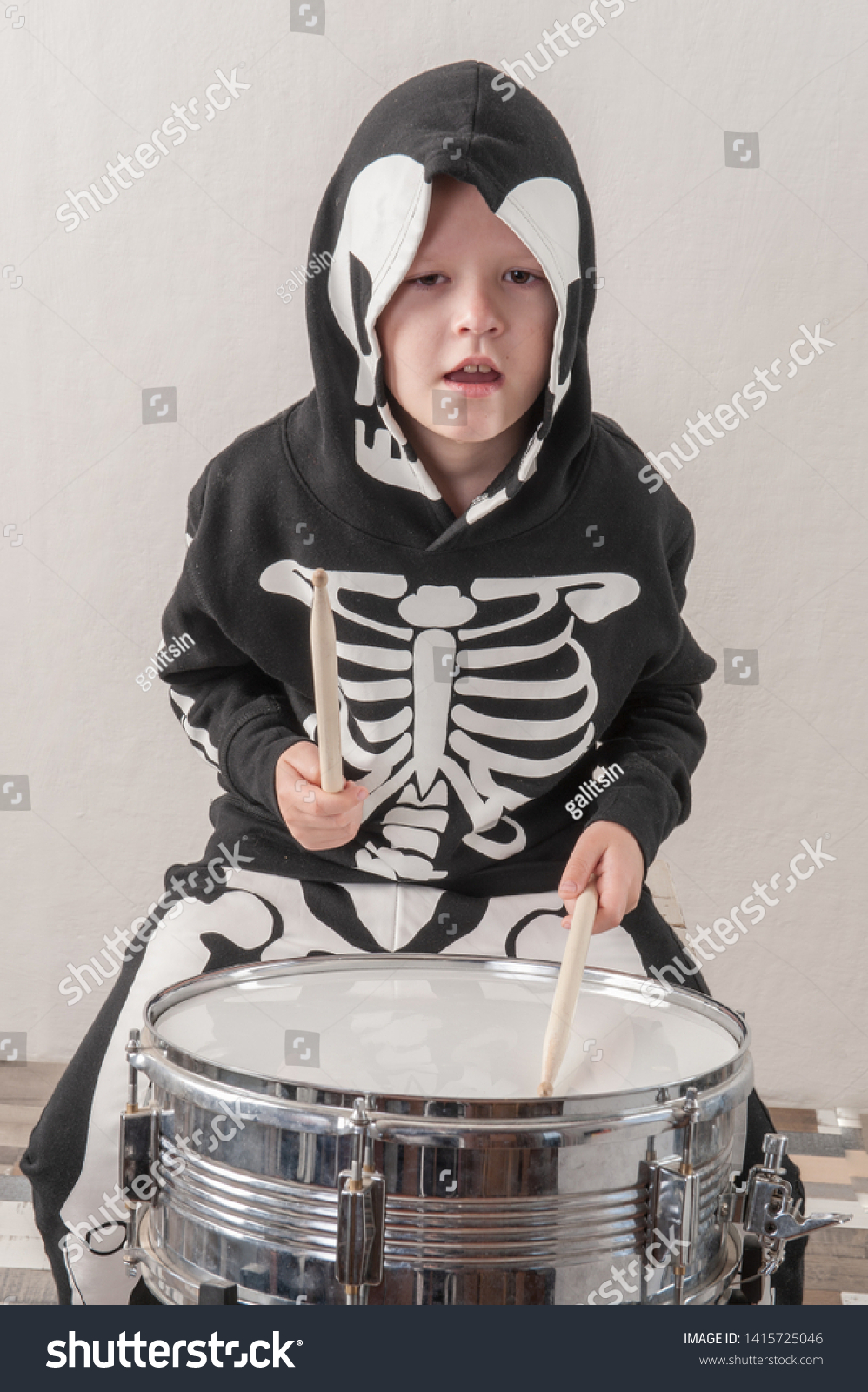 Happy friendly family of musicians in carnival costumes, boys and young mother play drum and try to sing with microphone. Black suit with image of skeletons. Classic halloween costume. Funny children #1415725046