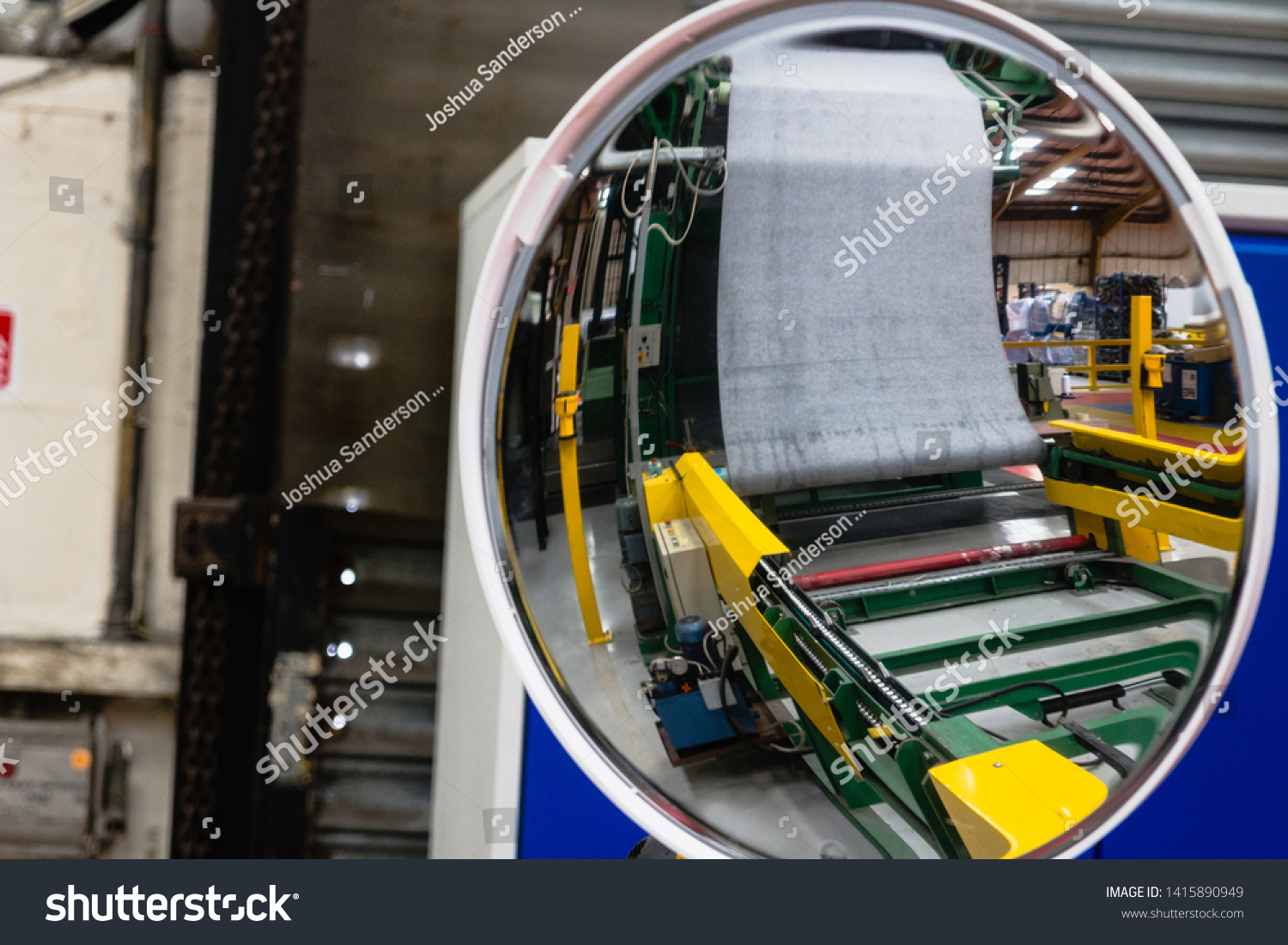 Curved circular mirror reflecting the inside of a factory for industry and production with bright reds, yellow, curved skylight reflection with photographer in the reflection worker health and safety #1415890949
