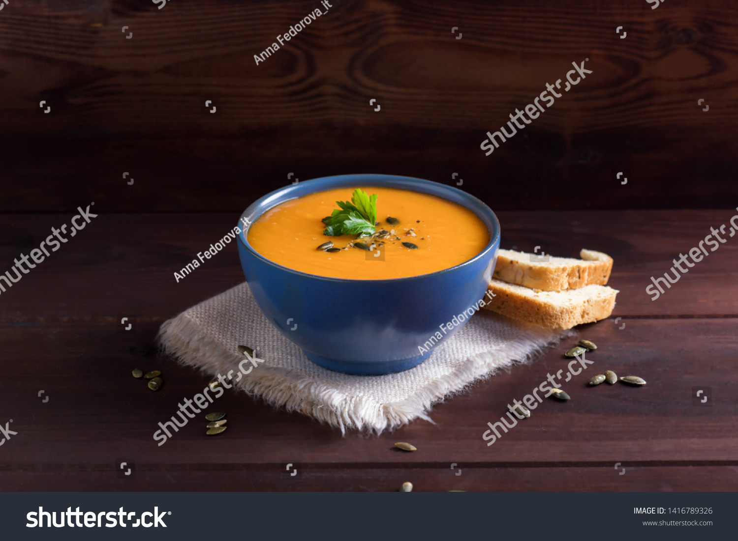 Pumpkin vegan soup in a blue bowl served with parsley, olive oil and pumpkin seeds and bread on a dark wooden background #1416789326