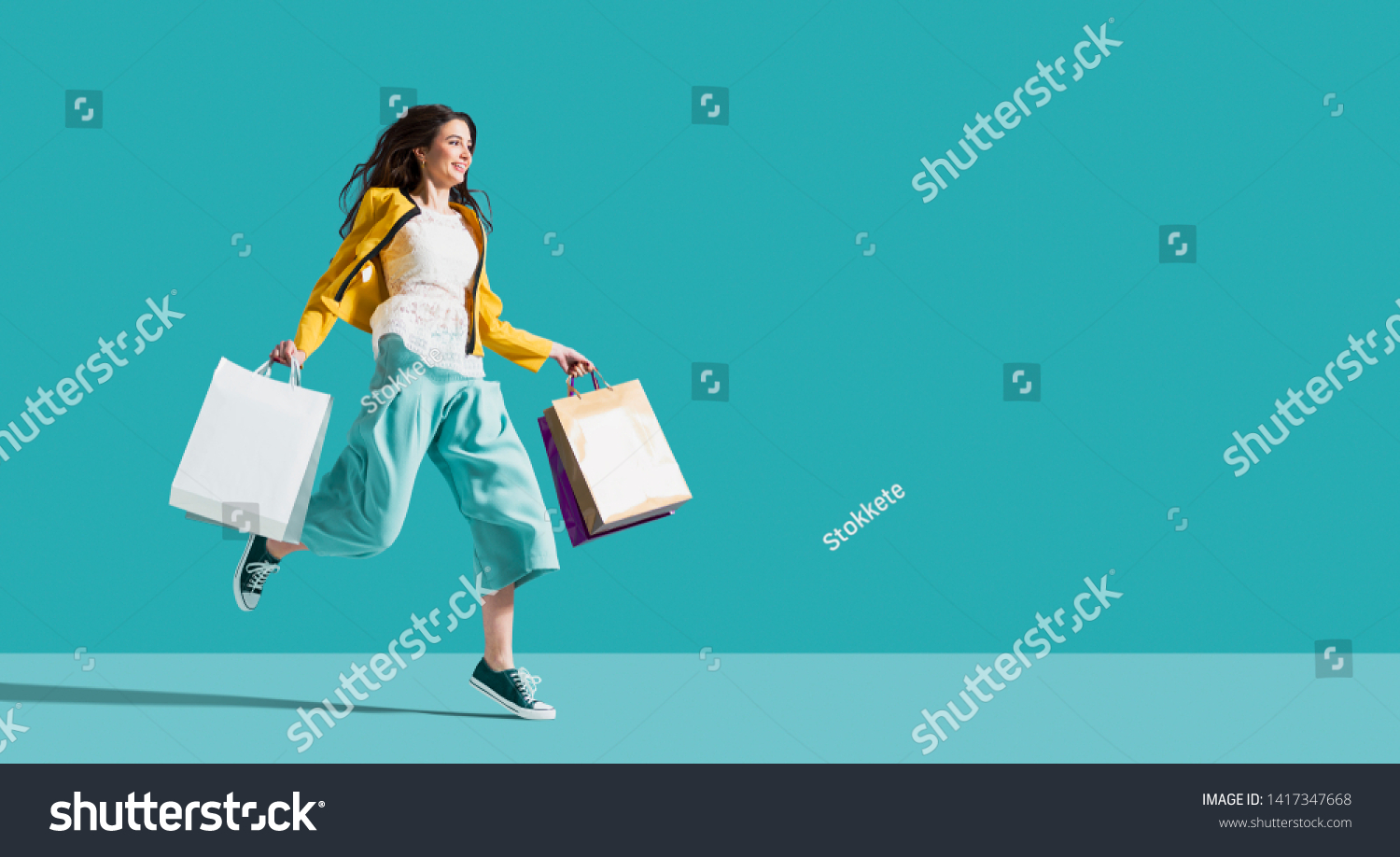 Cheerful happy woman enjoying shopping: she is carrying shopping bags and running to get the latest offers at the shopping center #1417347668