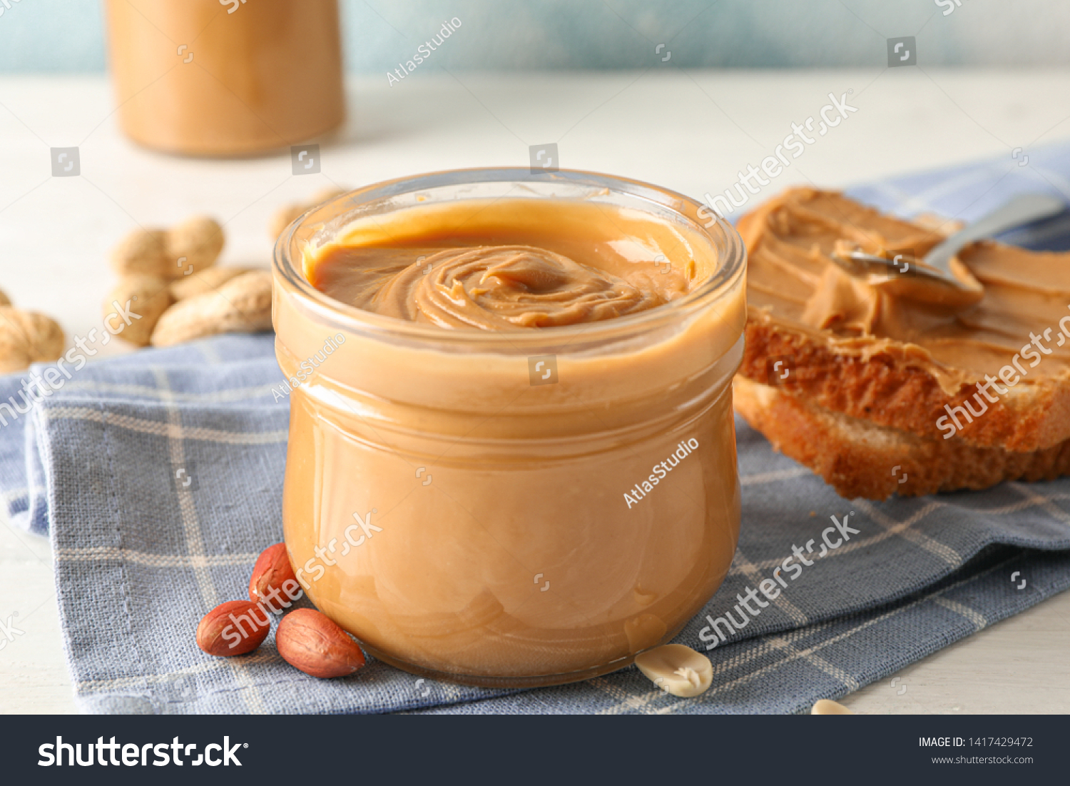 Glass jar with peanut butter, peanut, kitchen towel, spoon and peanut butter sandwich on white wooden background, space for text and closeup #1417429472