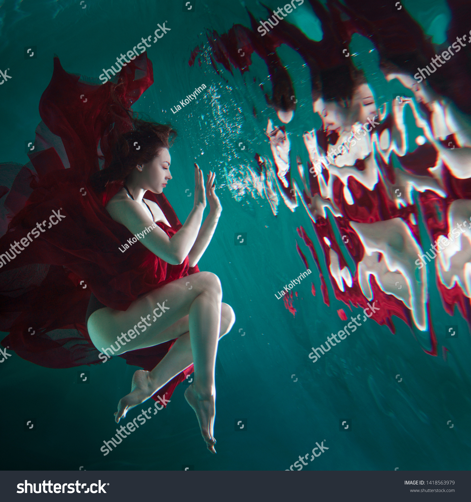 Mystical underwater portrait of a beautiful young woman in a red dress. The girl swims under the surface of the water and her reflection, Immersion concept #1418563979