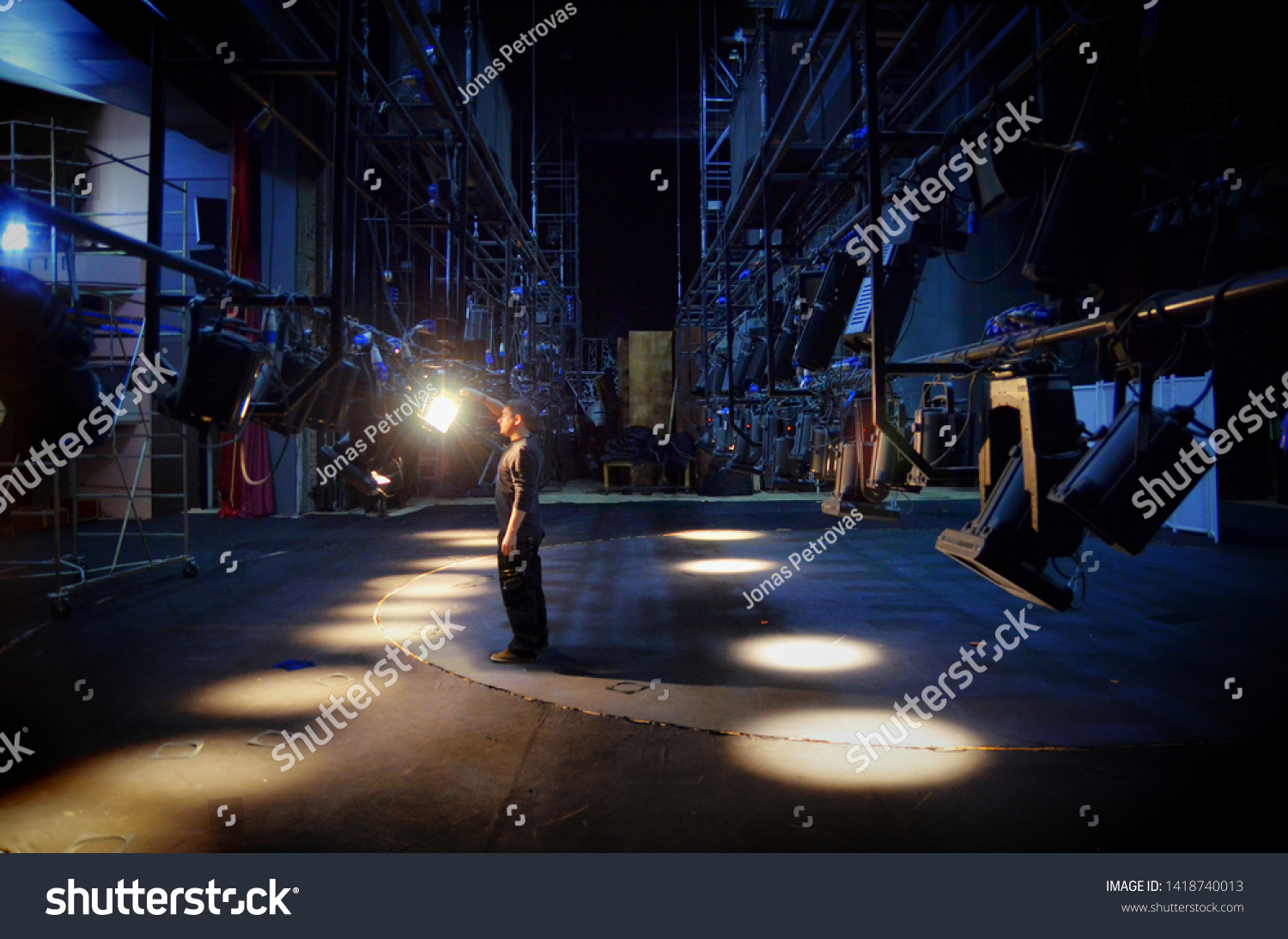 A young guy mounts lighting equipment on the stage of the theater #1418740013