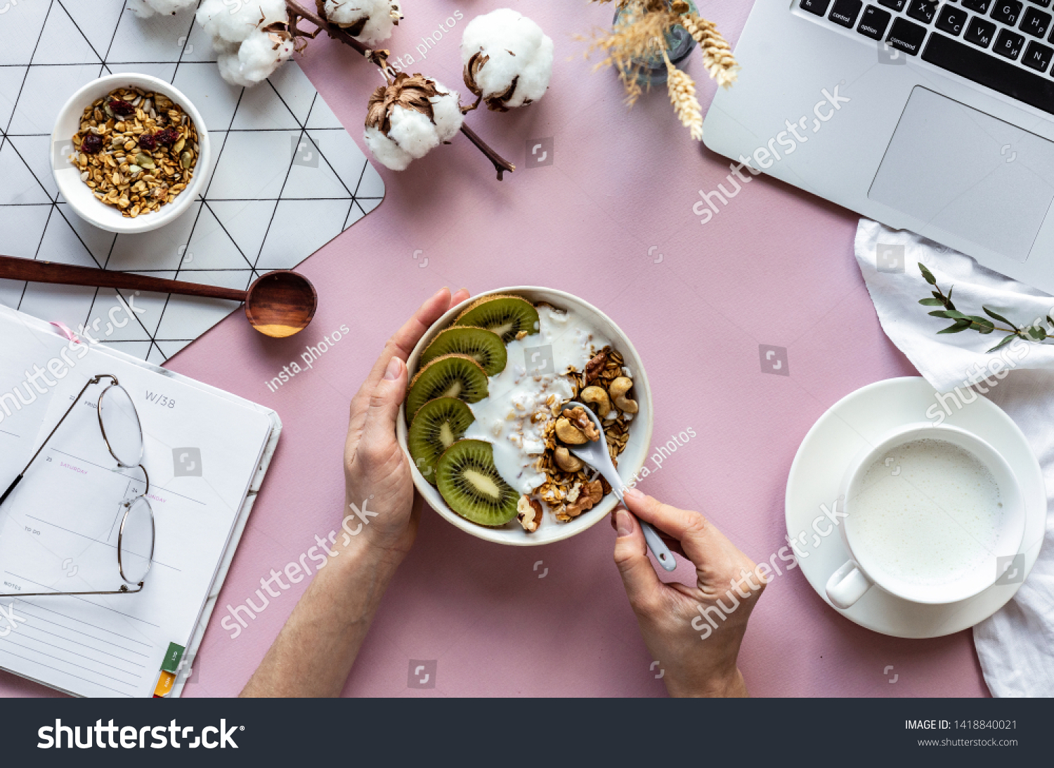 Female hand hold spoon over healthy breakfast concept bowl enjoy detox morning meal on work table background with laptop milk, woman eat natural granola nutrition detox food in home office, top view #1418840021