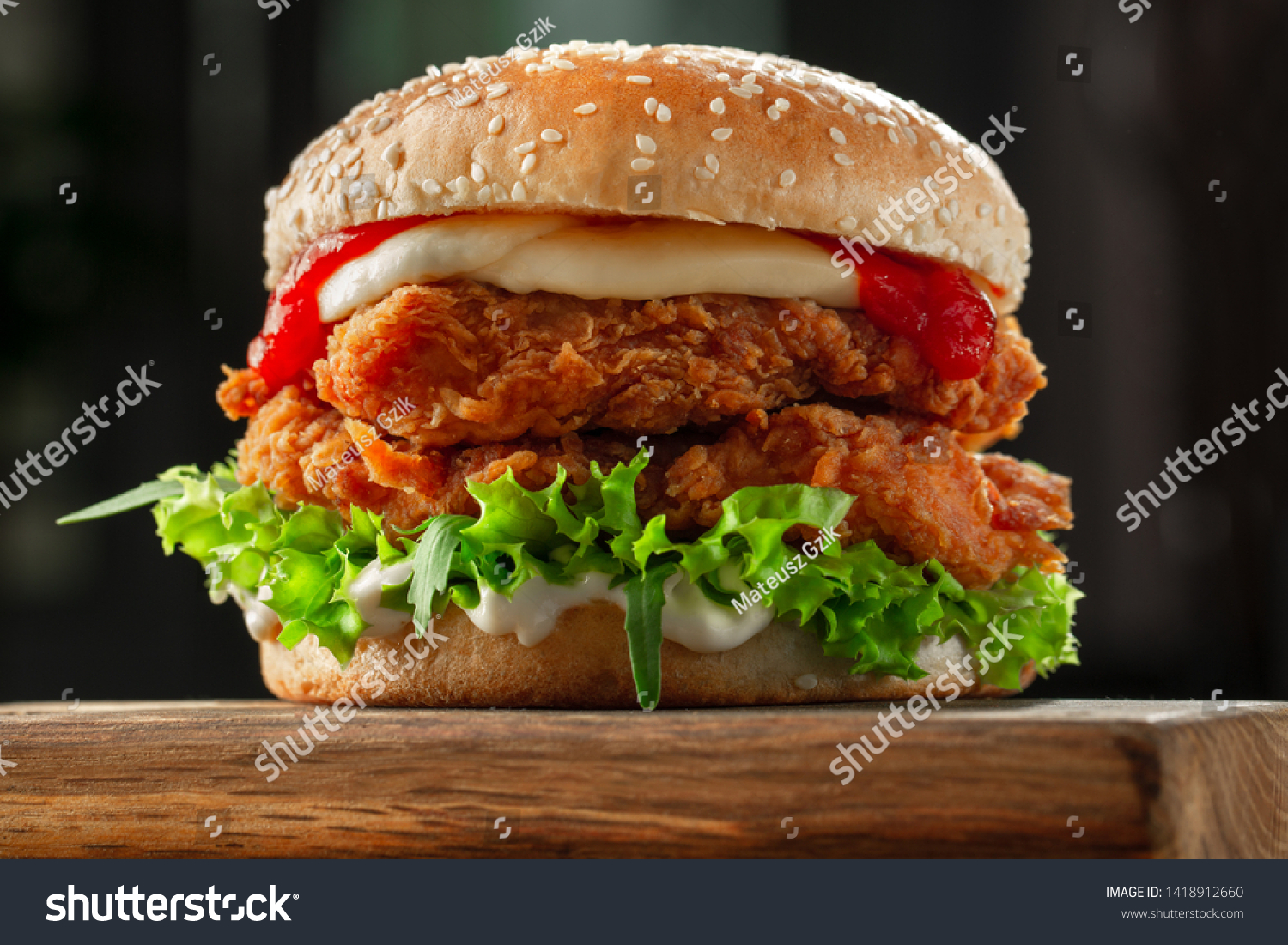 crispy, breaded chicken burger with mozzarella cheese standing on wooden cutting board #1418912660
