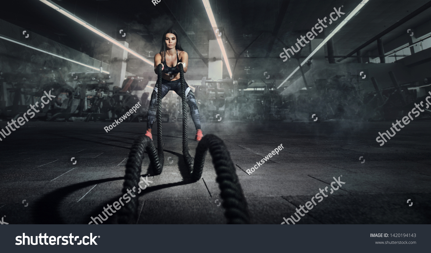 Sport. Battle ropes session. Attractive young fit sportswoman working out in functional training gym doing exercise with battle ropes. #1420194143