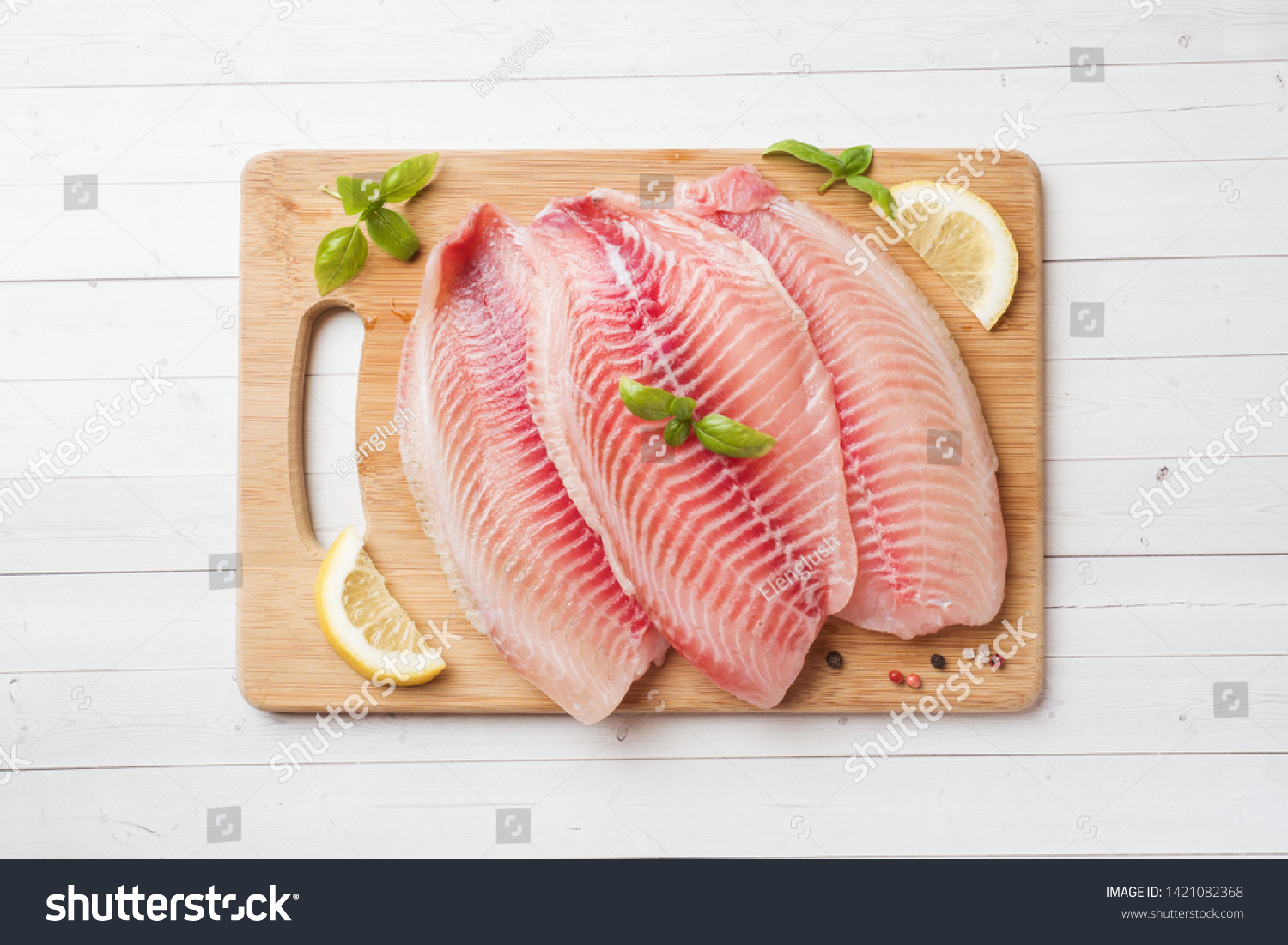 Raw fish fillet of tilapia on a cutting Board with lemon and spices. White table with copy space #1421082368