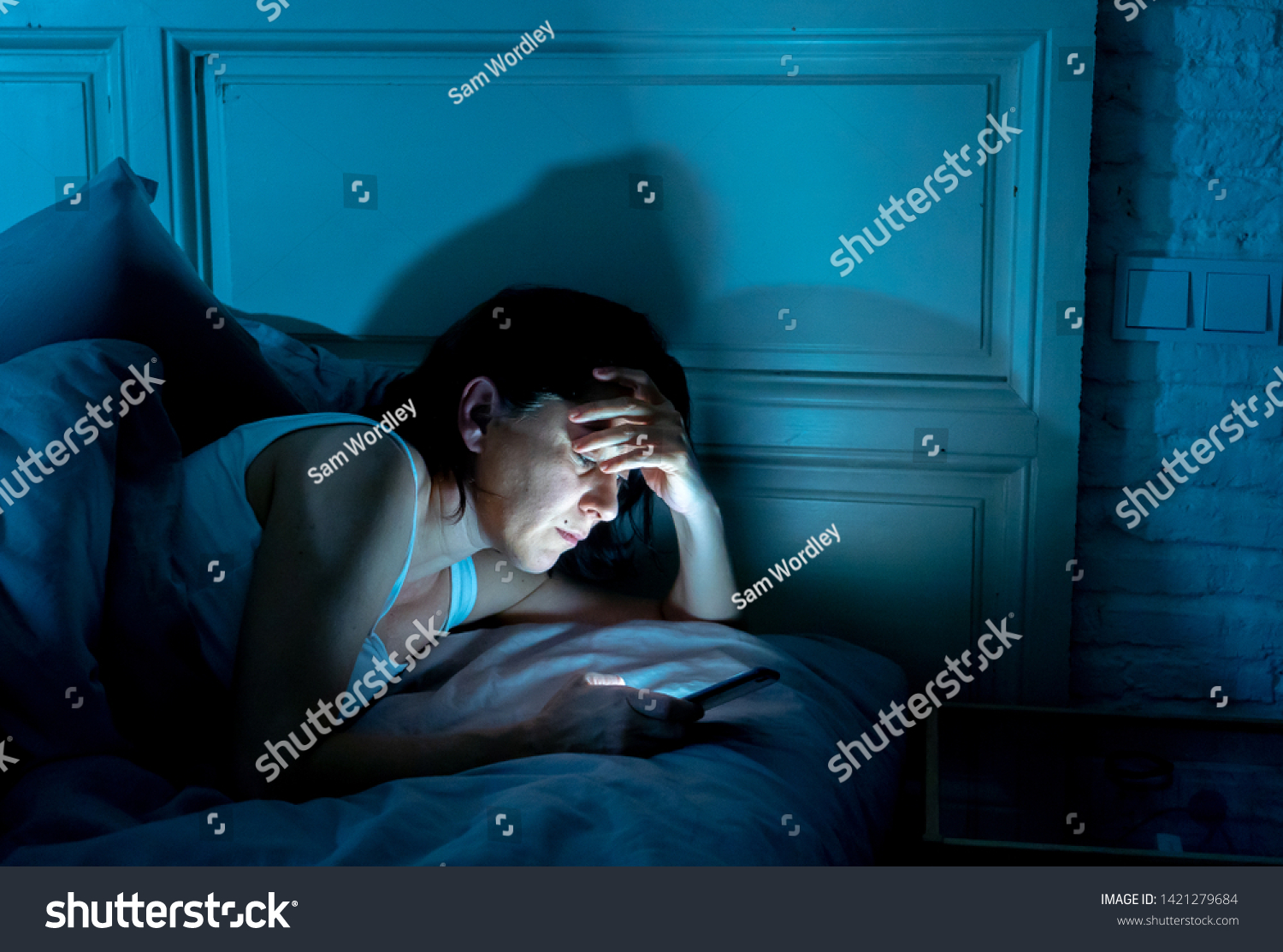 Young attractive woman awake late at night using smart phone lying in bed in a dark bedroom. Using mobile for chatting and sending messages in internet addiction, mobile abuse and insomnia concept #1421279684