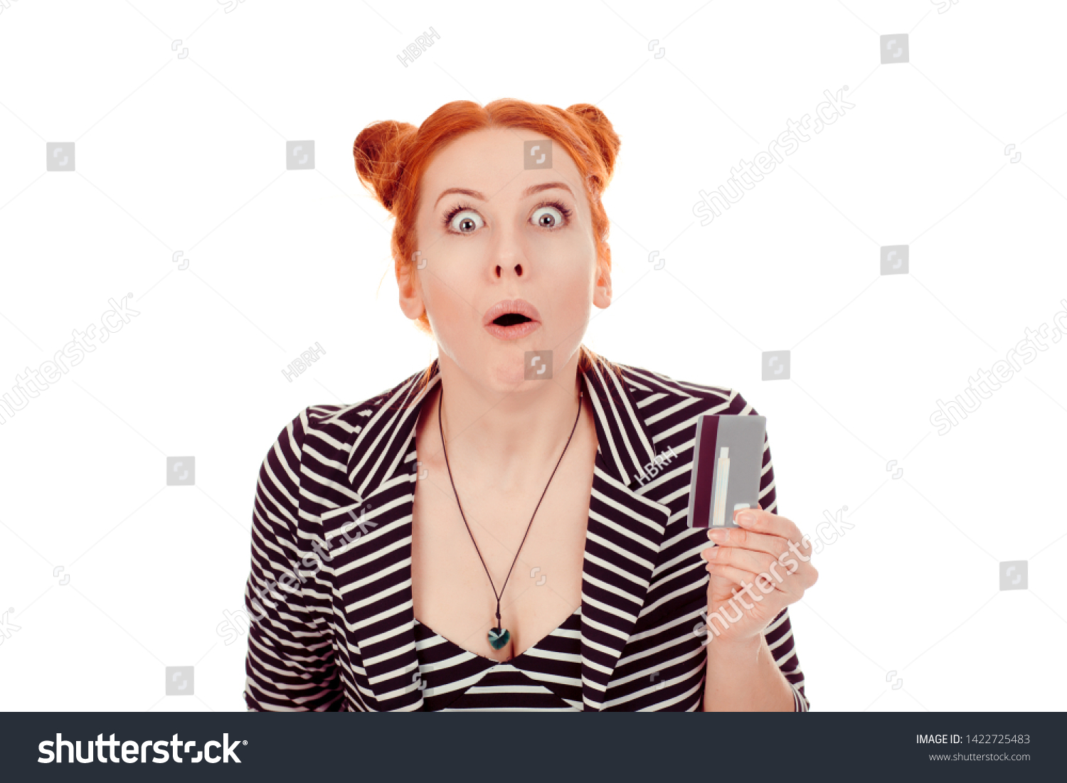Banking shocking news. Closeup portrait of a beautiful woman shocked stunned young girl showing credit card wearing striped black white jacket with 2 buns up hairdo isolated on white background wall #1422725483