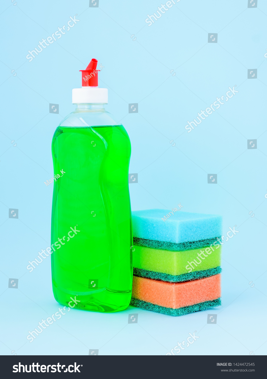 Transparent bottle with green dishwashing liquid and three foam sponges of different colours on a blue background. Kitchen detergent. Household chemicals. Household chores. #1424472545