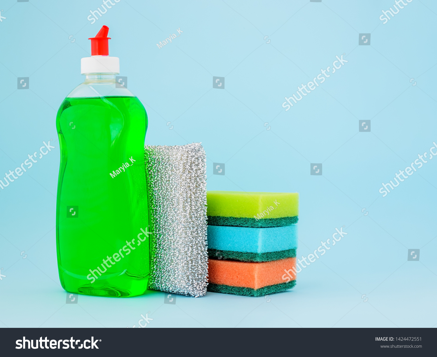 Transparent bottle with green dishwashing liquid and four foam sponges of different colours on a blue background. Copy space. Kitchen detergent. Household chemicals. Household chores. #1424472551