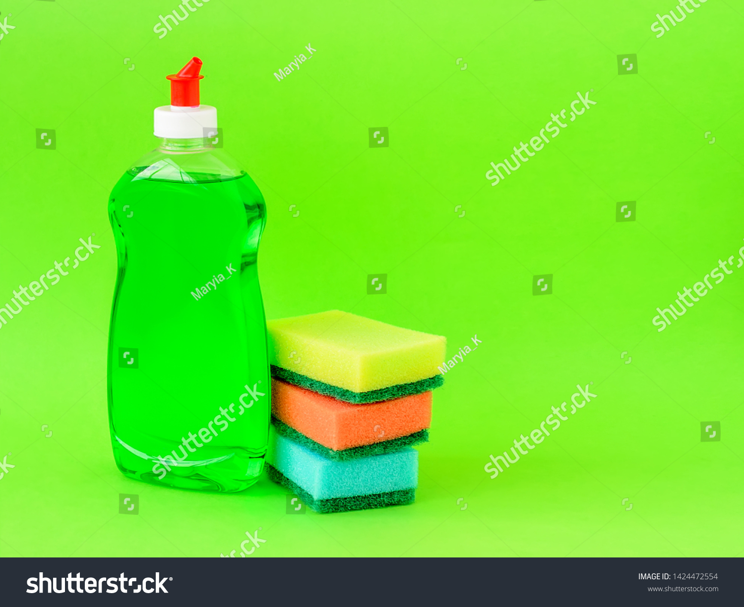 Transparent bottle with green dishwashing liquid and three foam sponges of different colours on a green background. Copy space. Kitchen detergent. Household chemicals. Household chores. #1424472554