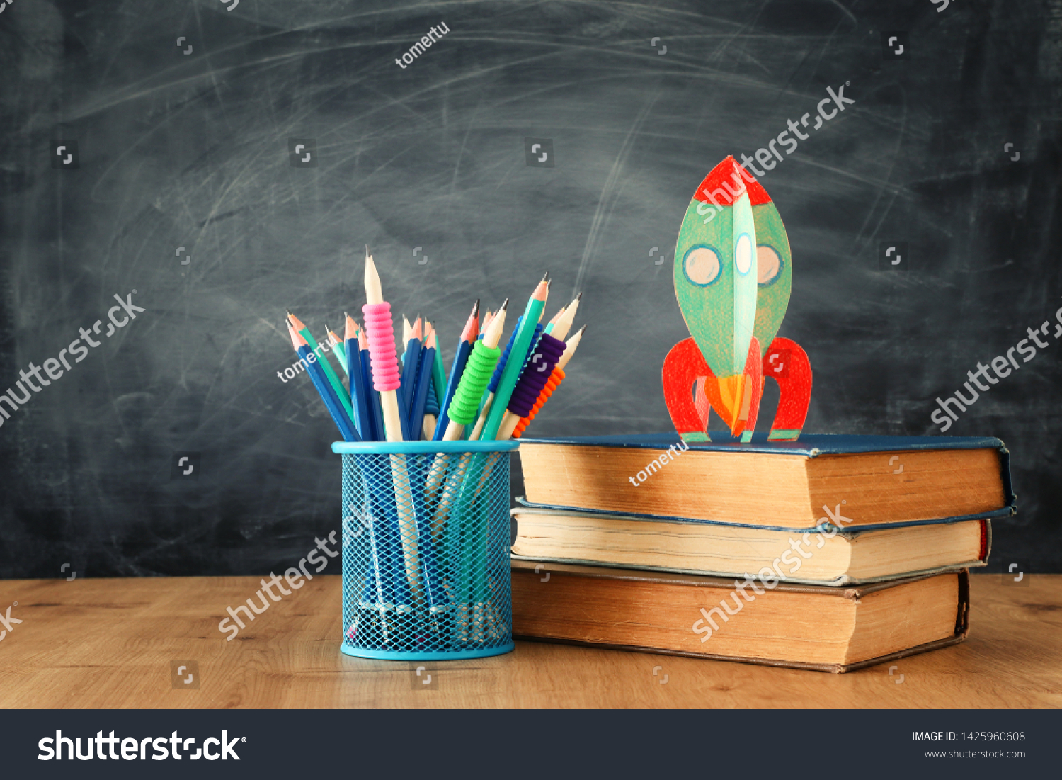 education and back to school concept. cardboard rocket and pencils over books in front of classroom blackboard #1425960608