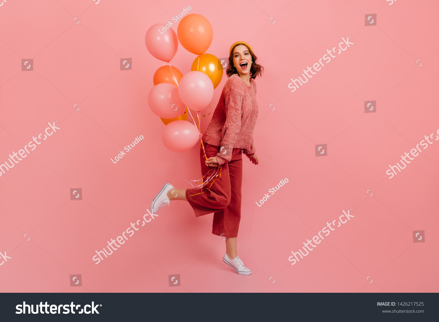 Full length view of joyful lady jumping with air balloons. Studio shot of laughing birthday girl posing on pink background. #1426217525