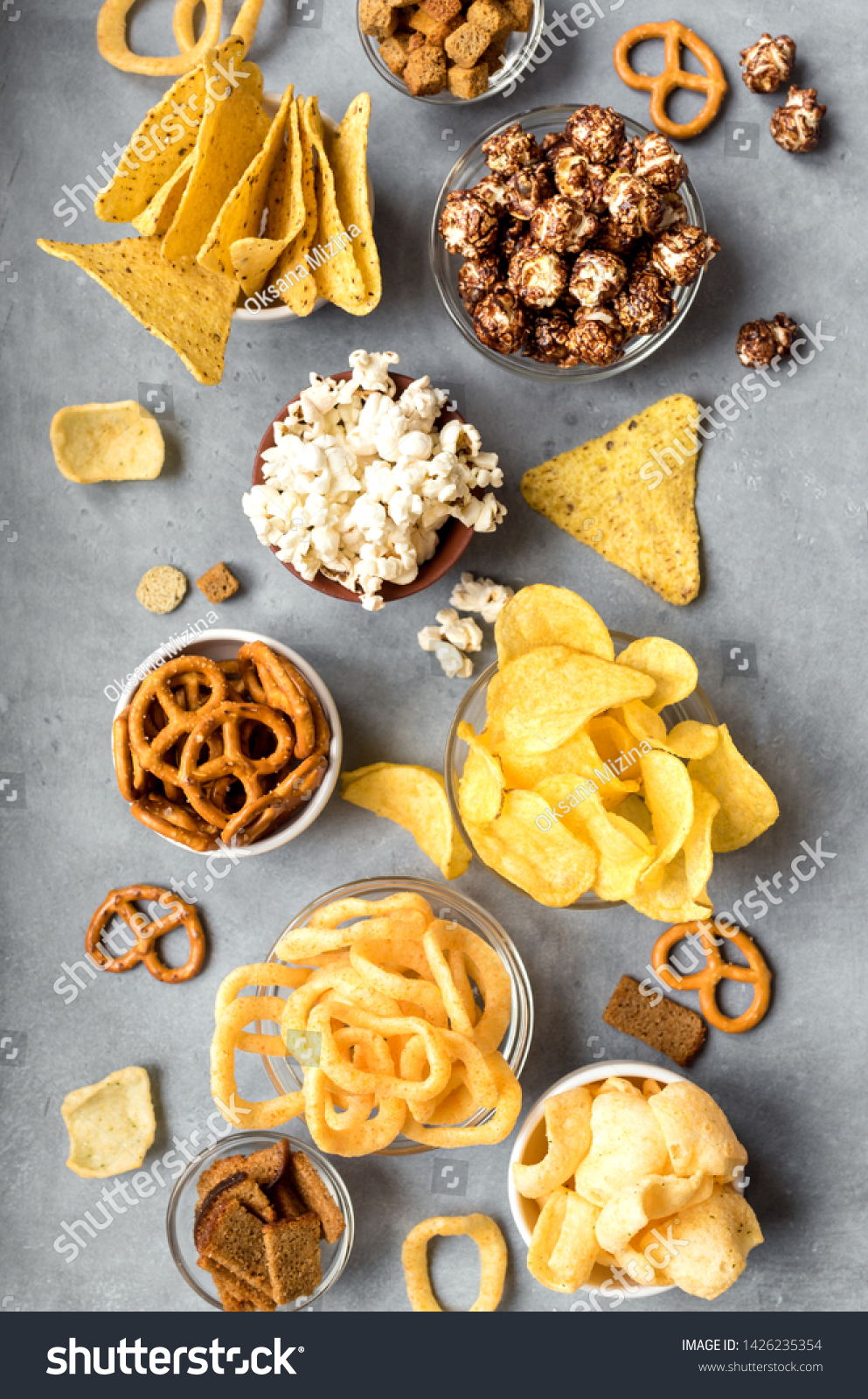 Assortment of Unhealthy Snacks: chips, popcorn, nachos, pretzels, onion rings in bowls, top view, flat lay. Unhealthy eating concept. #1426235354