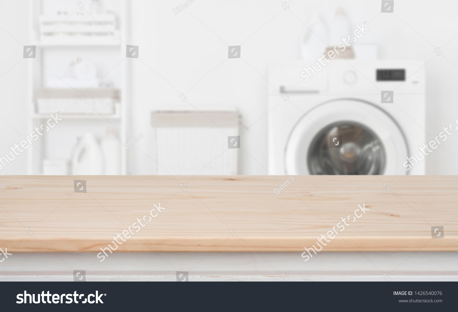 Wooden table in front of defocused washing machine and laundry #1426540076