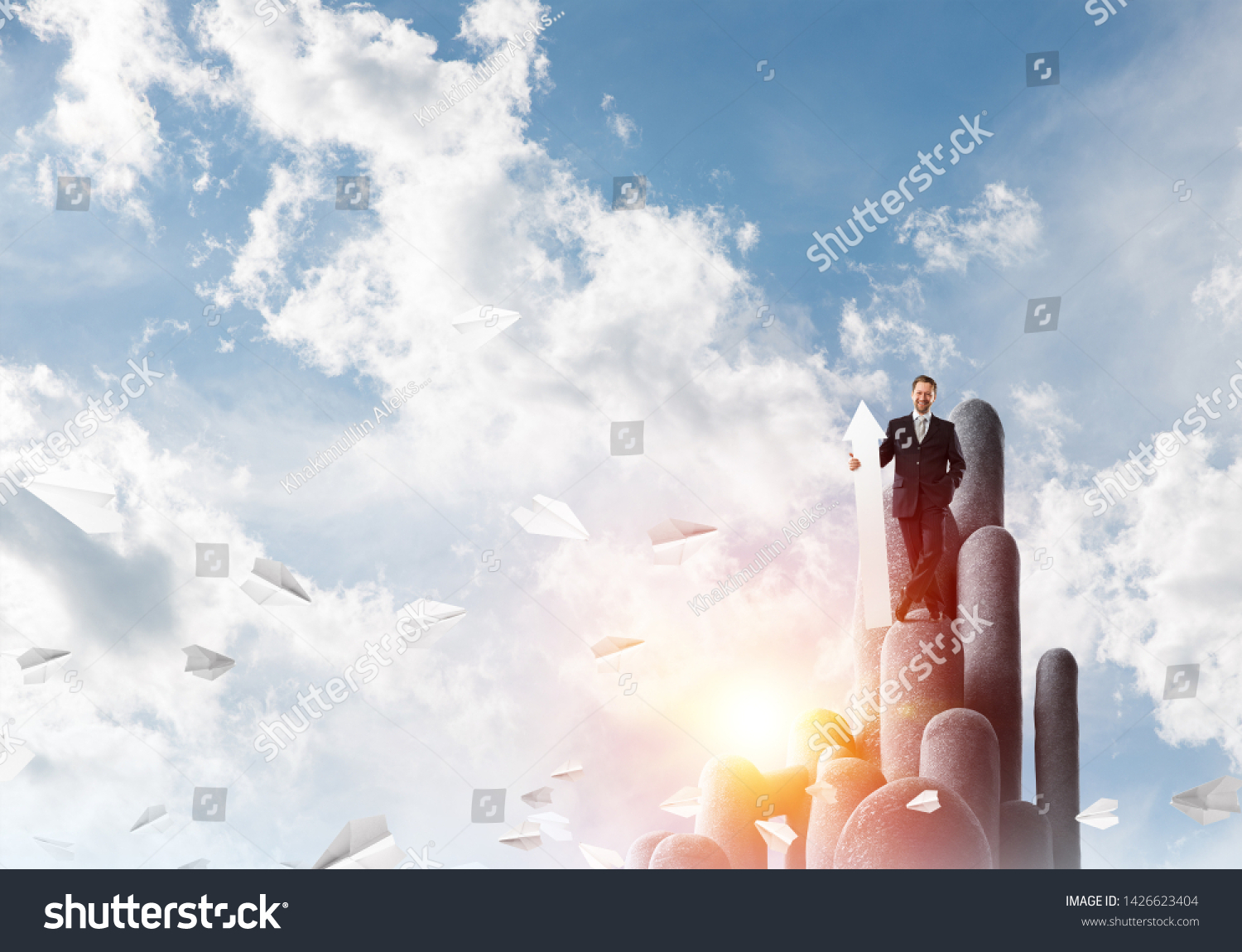 Ambitious and young businessman in suit holding big white banner in hand while standing on stune column with cloudy skyscape view on background #1426623404