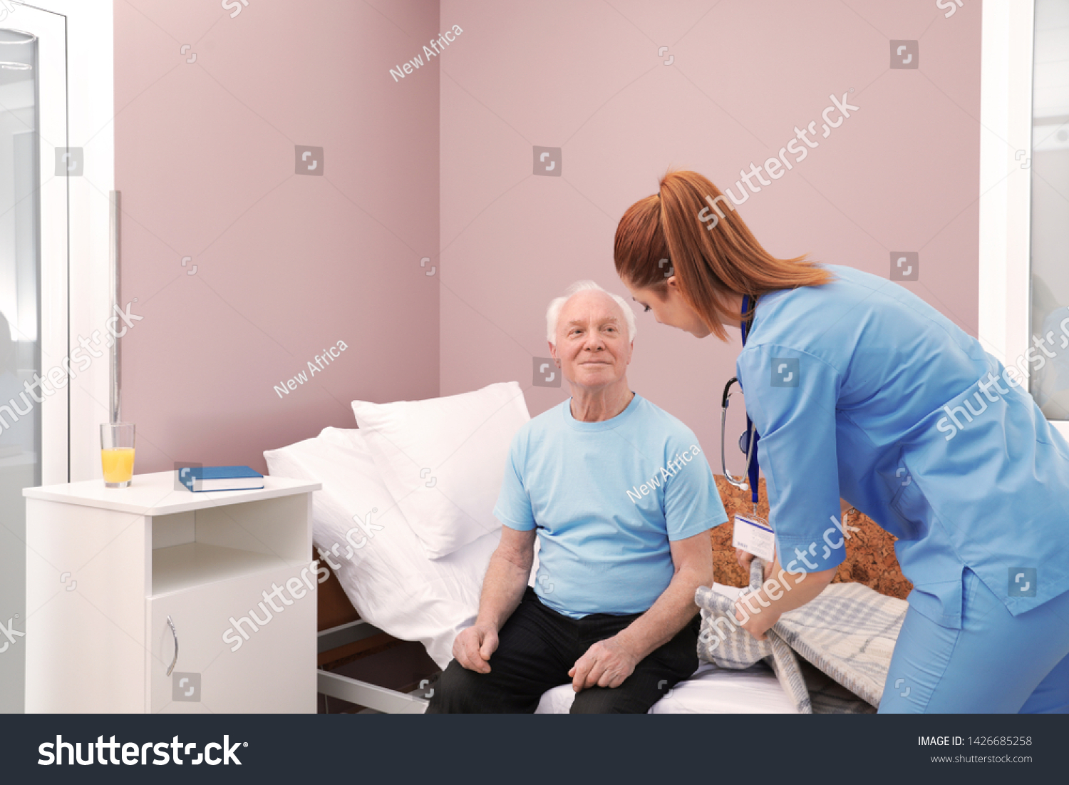 Nurse assisting senior man on bed in hospital ward #1426685258