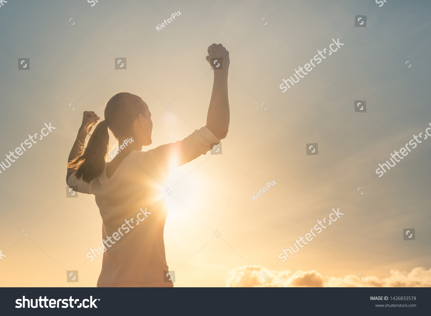 Strong woman, Winning, success , and life goals concept. Young woman with arms flexed facing the sunset.  #1426833578