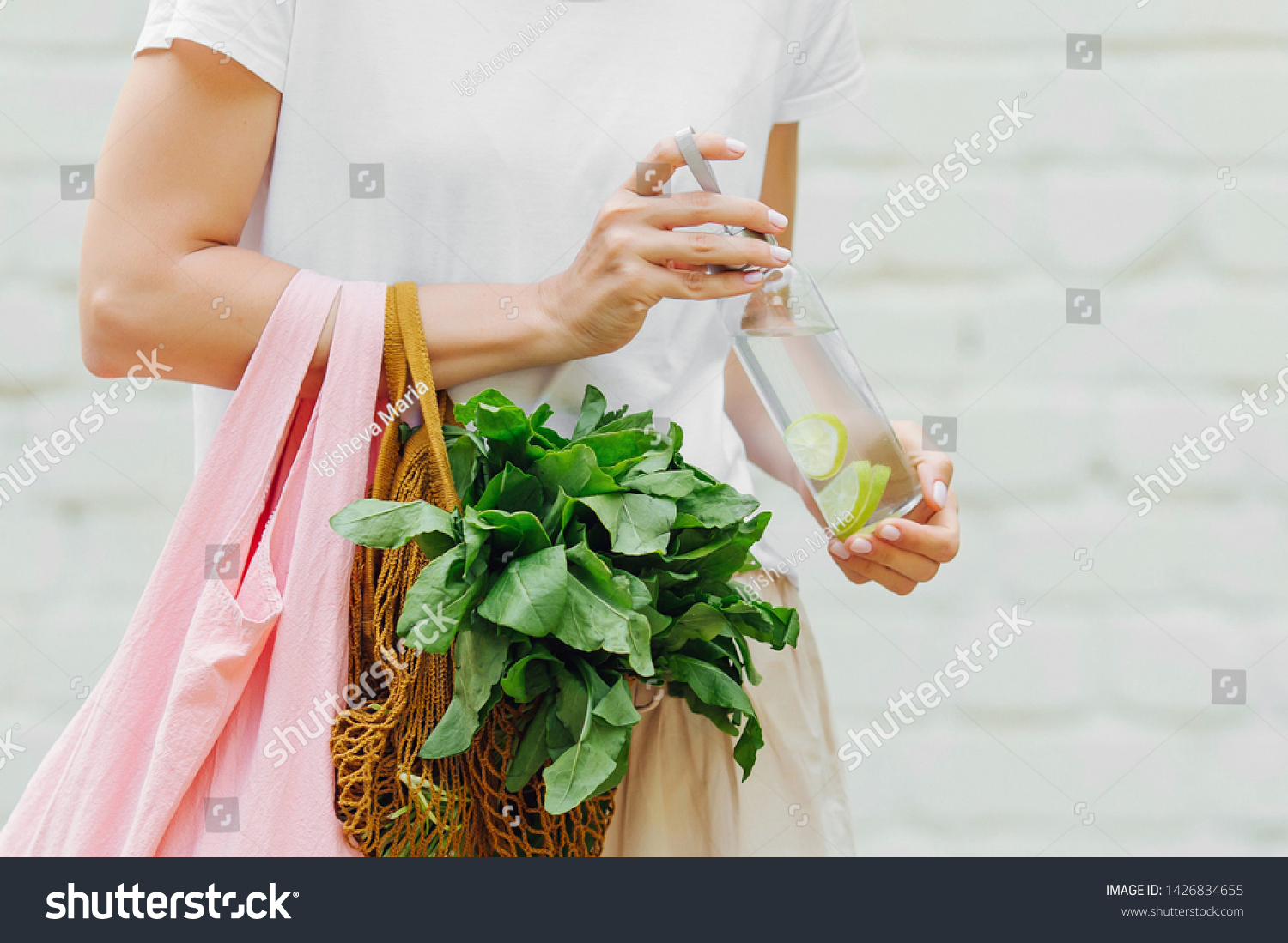 Female hands hold eco bag of vegetables, greens and reusable water bottle. Zero waste. Sustainable lifestyle concept. #1426834655