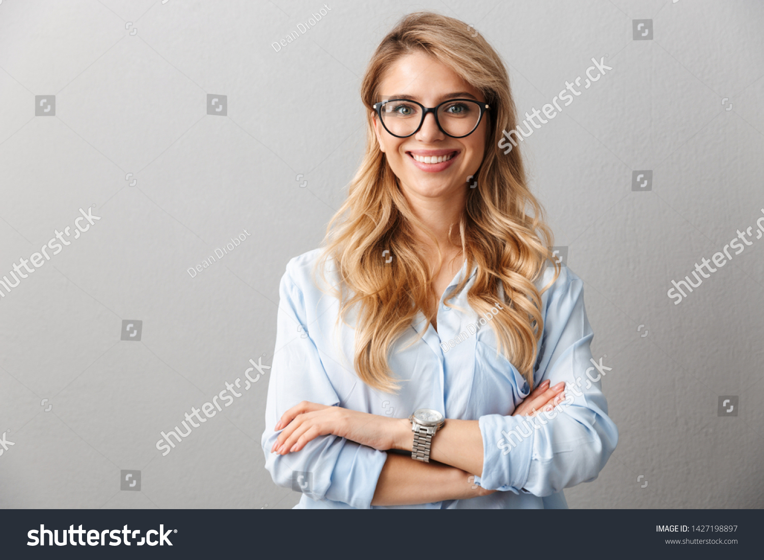 Photo of happy blond businesswoman wearing eyeglasses smiling and standing with hands crossed isolated over gray background #1427198897
