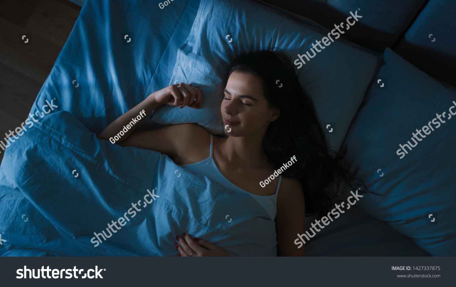 Top View of Beautiful Young Woman Sleeping Cozily on a Bed in His Bedroom at Night. Blue Nightly Colors with Cold Weak Lamppost Light Shining Through the Window. #1427337875