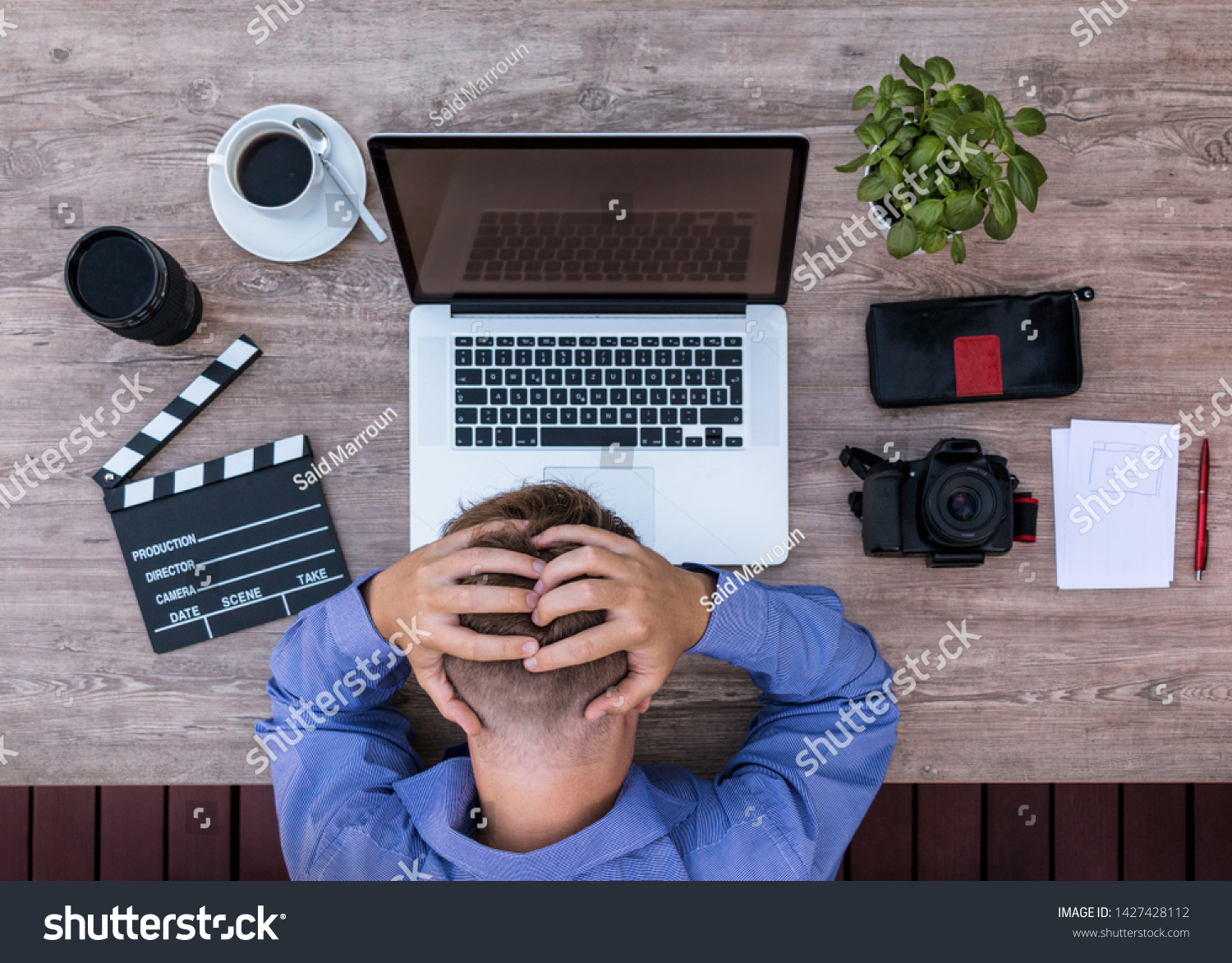 Man in a bad mood holding his head with his hands with technology gear on his desk, content creator burnout. #1427428112