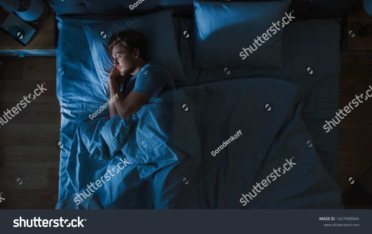 Top View of Handsome Young Man Sleeping Cozily on a Bed in His Bedroom at Night. Blue Nightly Colors with Cold Weak Lamppost Light Shining Through the Window. #1427499944