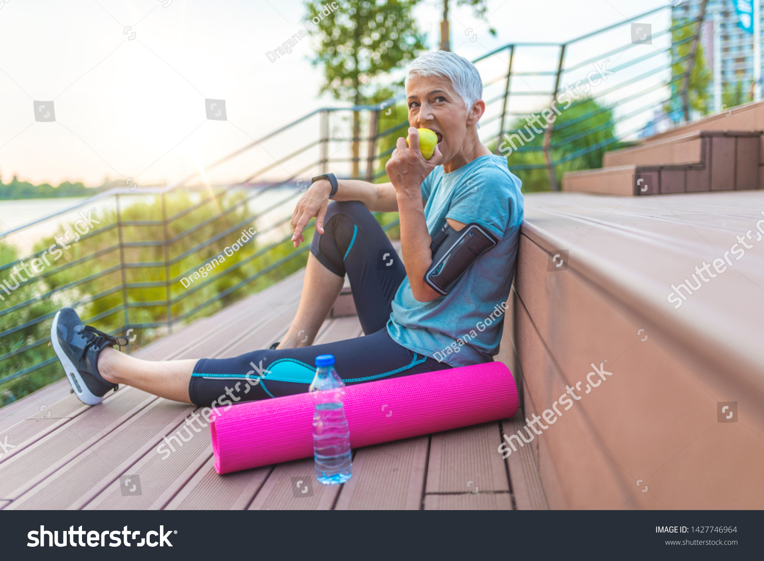 Sport mature woman sitting and resting after workout or exercise and eating apple on floor. Relax concept. Strength training and Body build up theme. Beautiful sporty woman eating apple #1427746964