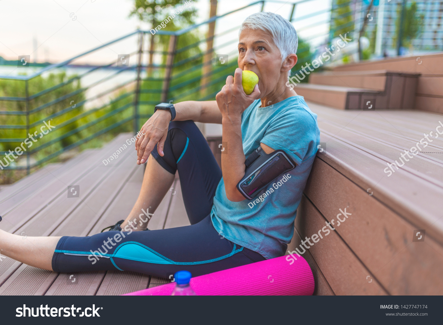 Beautiful sporty senior woman eating apple.  Beautiful senior sports lady smiling, holding an apple. Caucasian beautiful healthy athletic sportive senior woman eat green apple  #1427747174