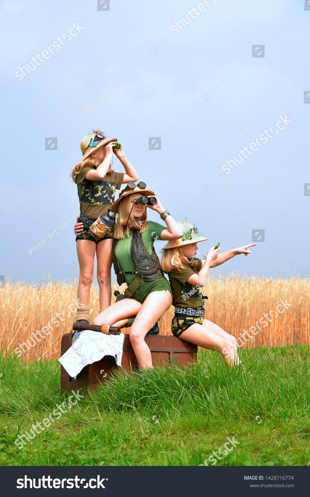 Twin young sisters and an adult girl dress up as explorers.
They pose in the outdoors dressed with jungle hats and
khaki safari clothes. #1428716774