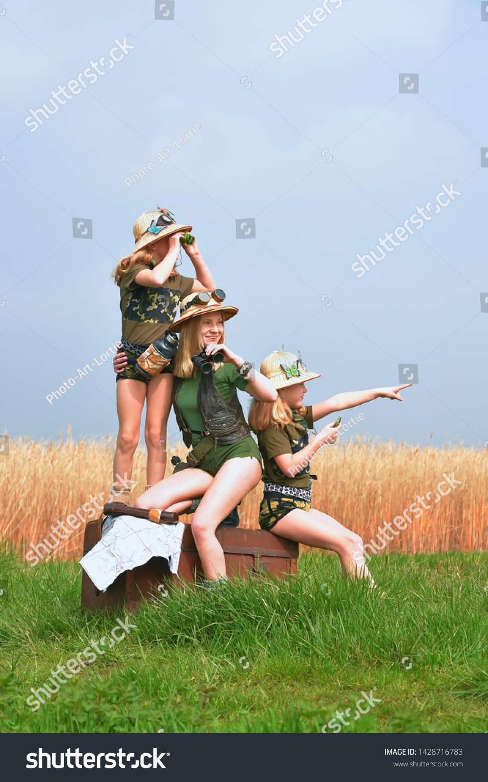 Twin young sisters and an adult girl dress up as explorers.
They pose in the outdoors dressed with jungle hats and
khaki safari clothes. #1428716783