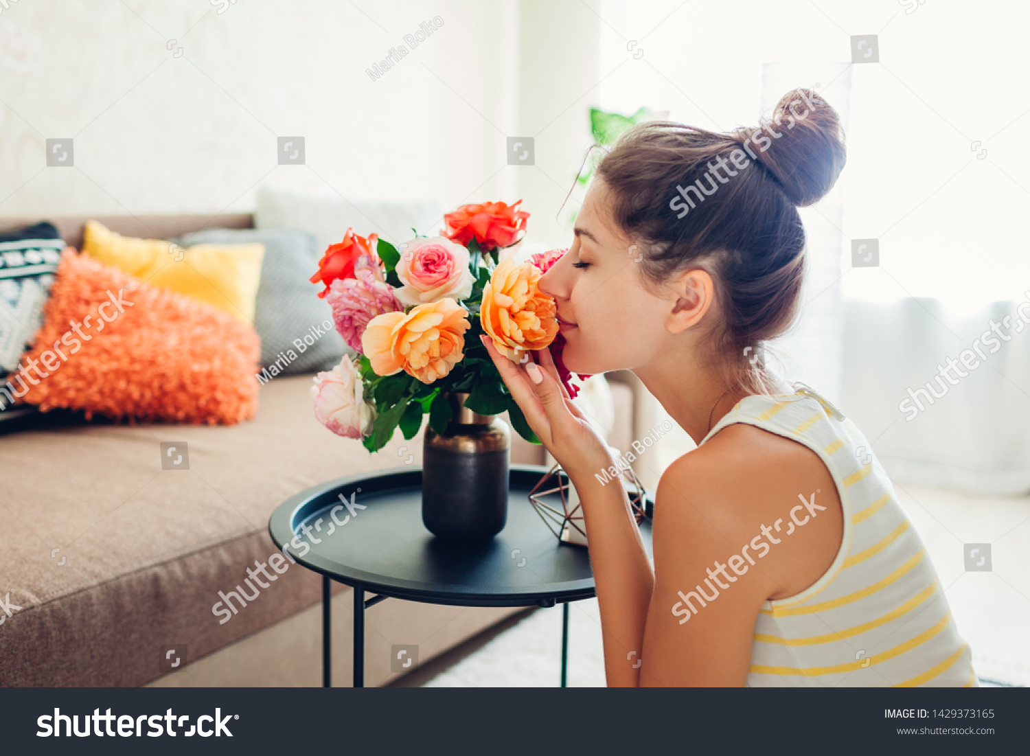 Woman smelling fresh roses in vase on table. Housewife taking care of coziness in apartment. Interior and decor #1429373165