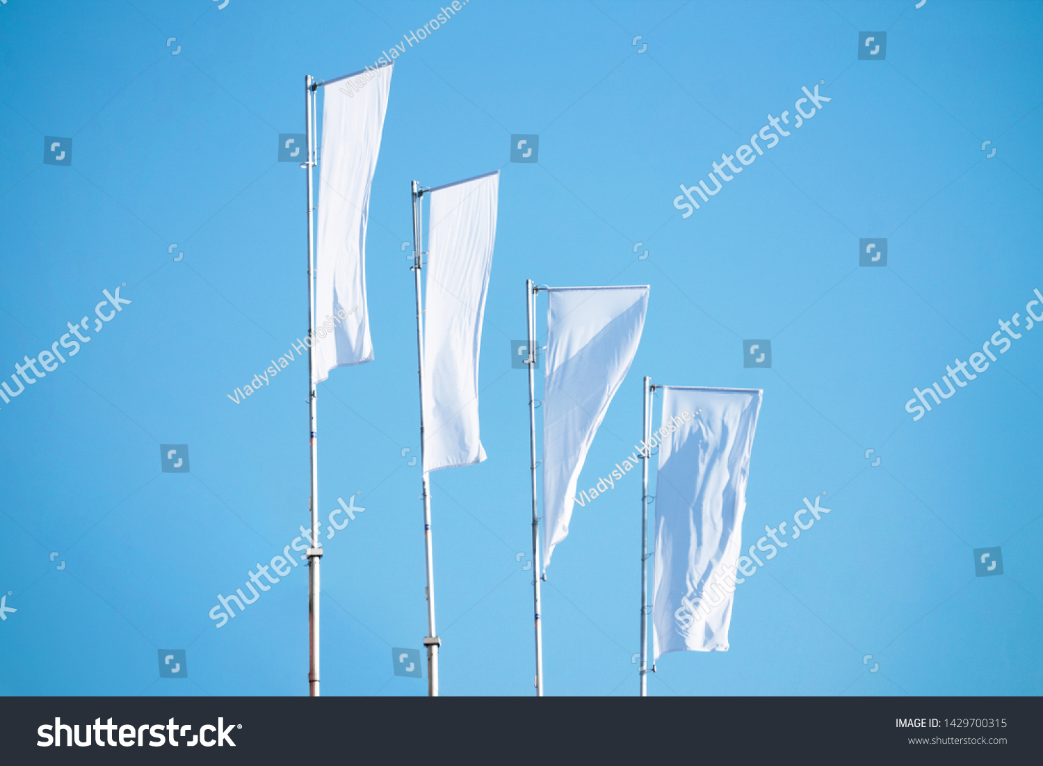 Three blank white flags on flagpoles against cloudy blue sky with perspective, corporate flag mockup to ad logo, text or symbol, company identity flag template with copy space #1429700315