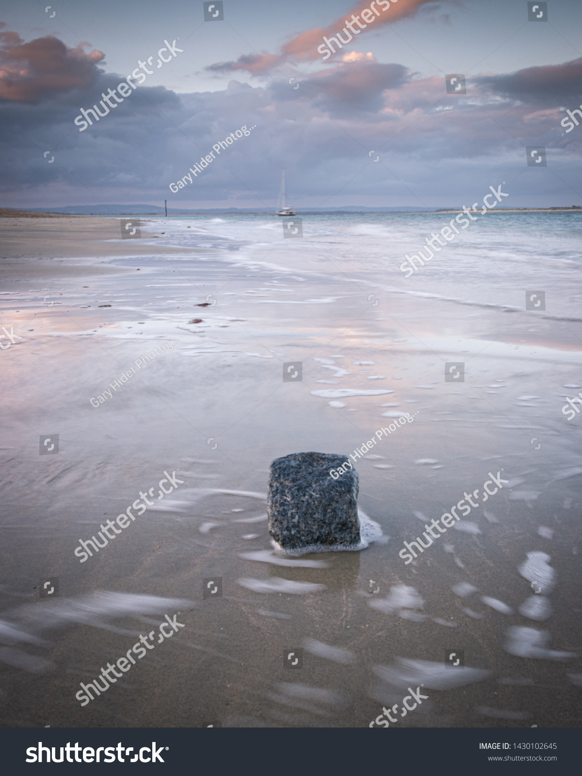 water swirling around a rock on a calm sandy beach at sunset  #1430102645