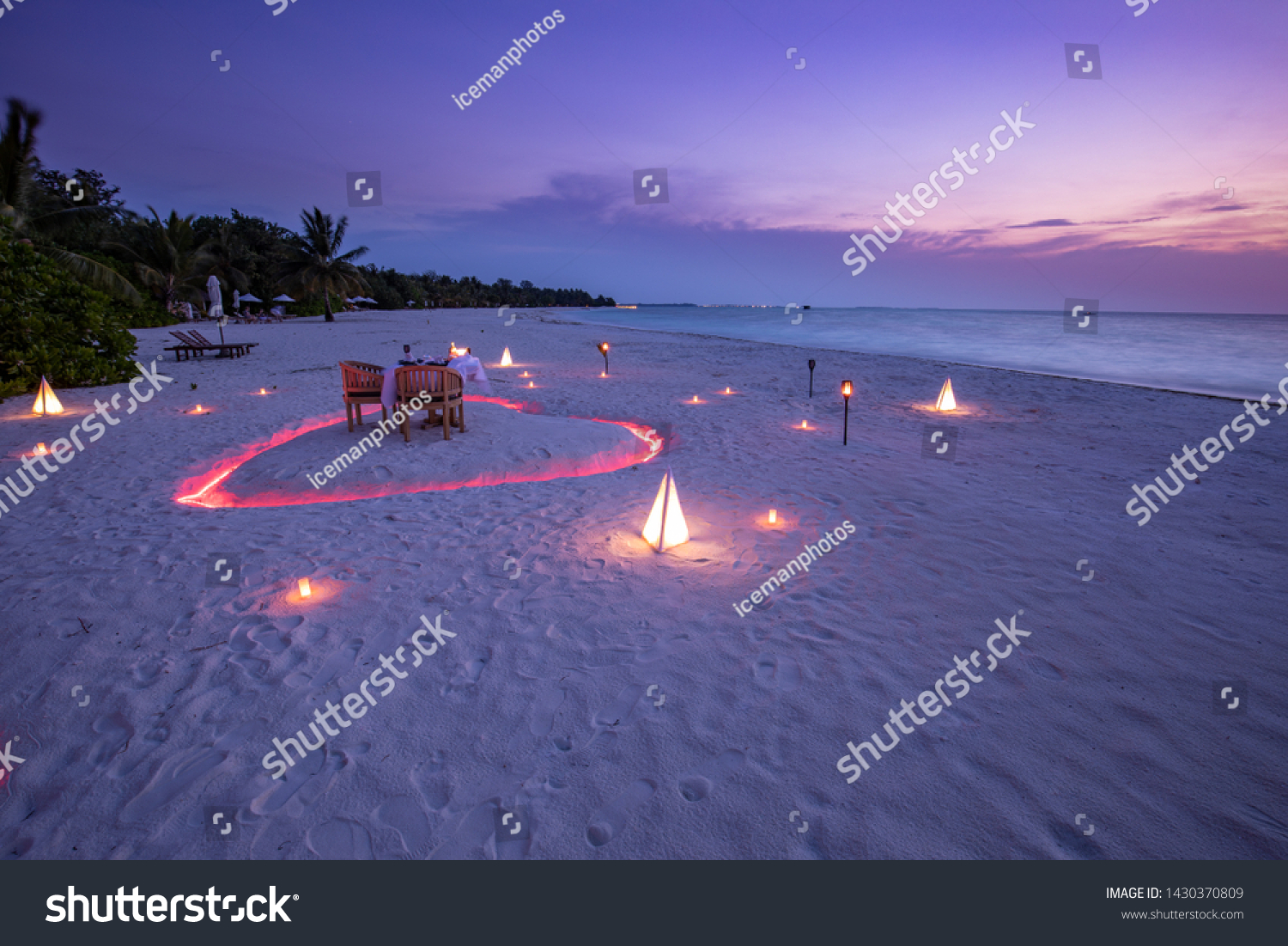 A young couple share a romantic dinner with candles heart shape close the sea sandy beach. Beautiful honeymoon destination, luxury travel, exotic beach dinner at sunset sky with sea background #1430370809