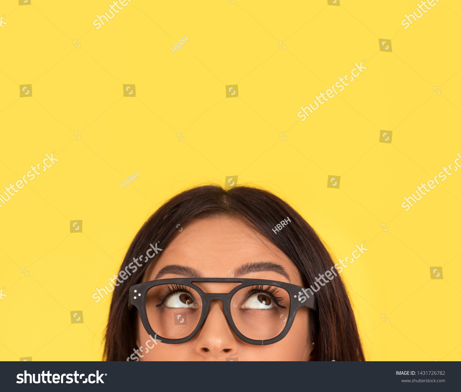 closeup portrait headshot cropped face above lips of cute happy woman in glasses looking up isolated on yellow studio wall background with copy space above head. Human face expressions, emotions #1431726782