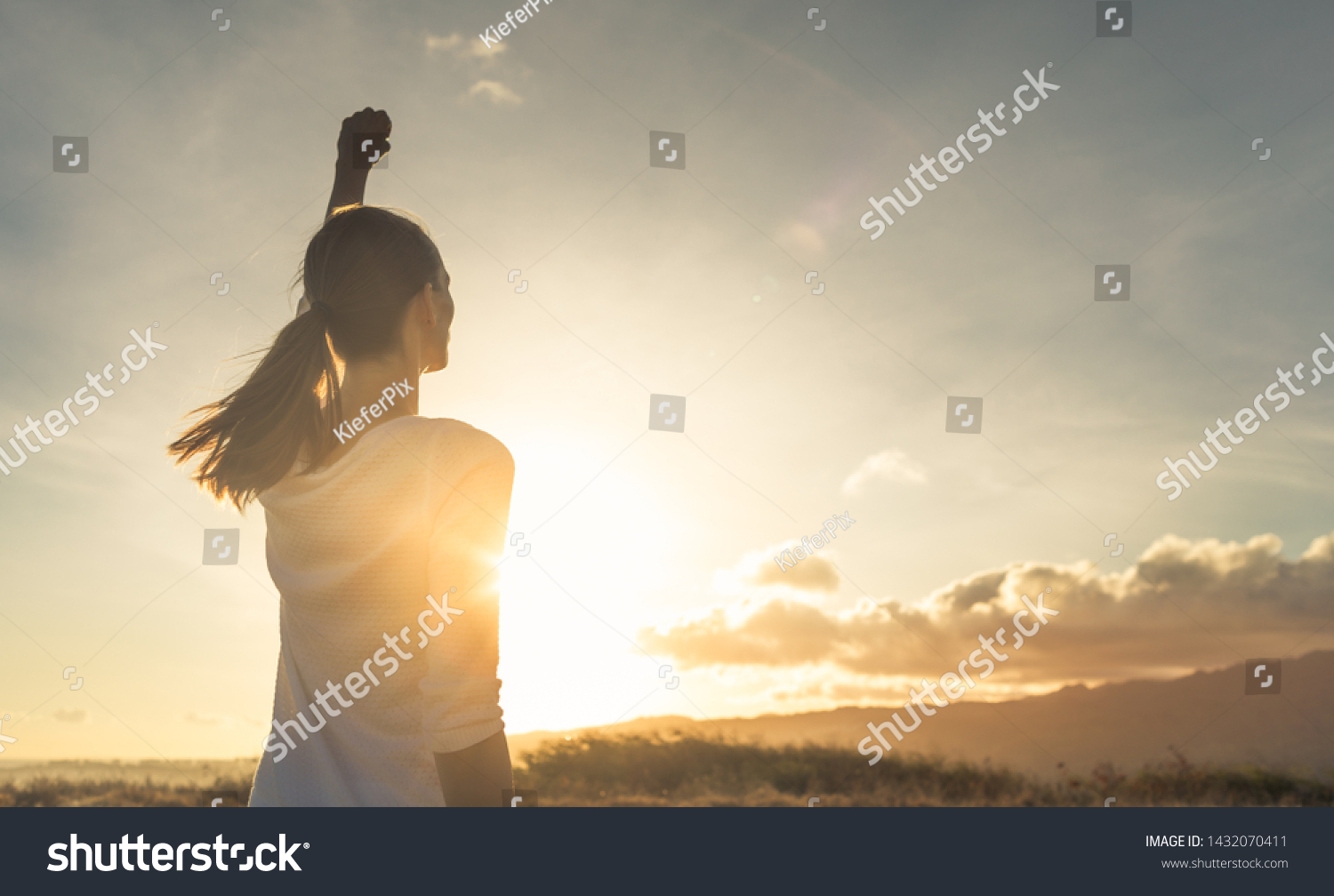 Strong, determined, confident woman with her fist up in the air facing sunset. #1432070411