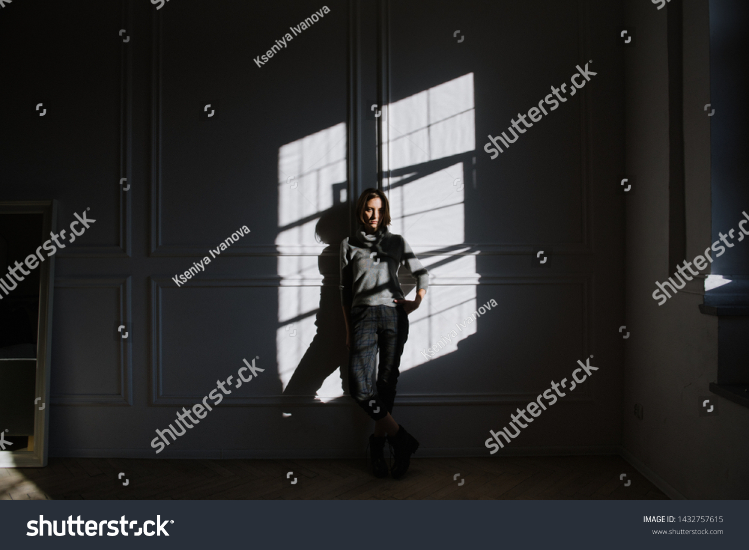 Beautiful young brunette woman in a gray sweater in the studio in the sun. Portraits of a young brunette woman en sun. #1432757615