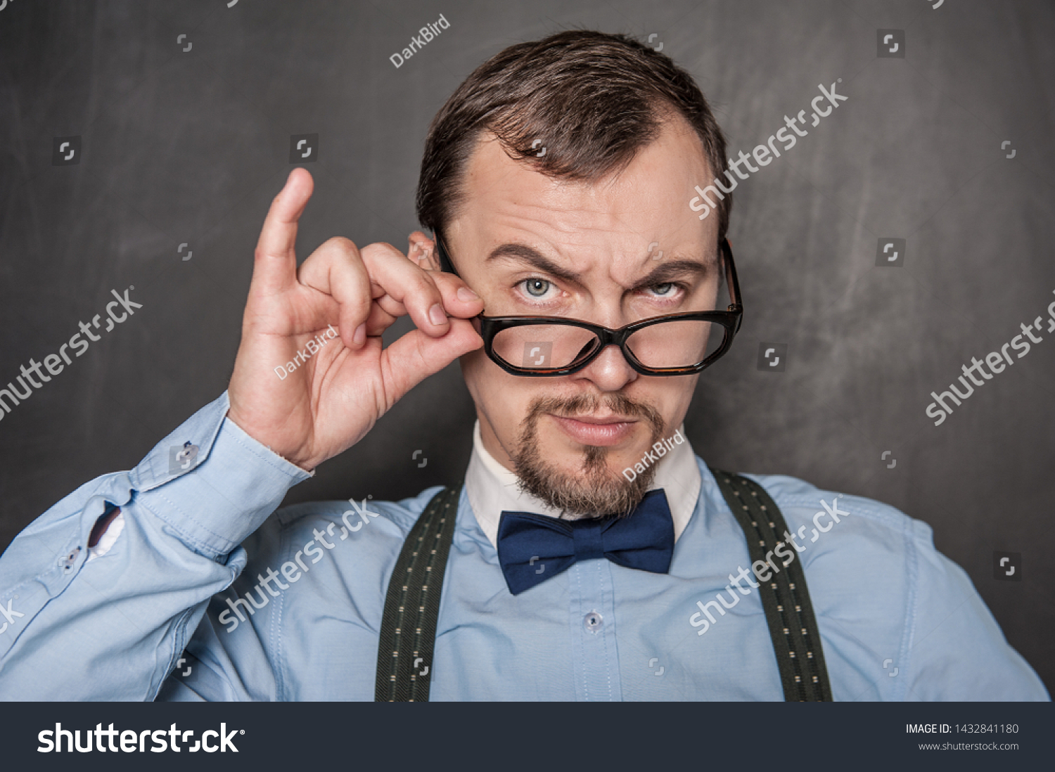 Handsome strict teacher in eyeglasses looking at you on blackboard background #1432841180