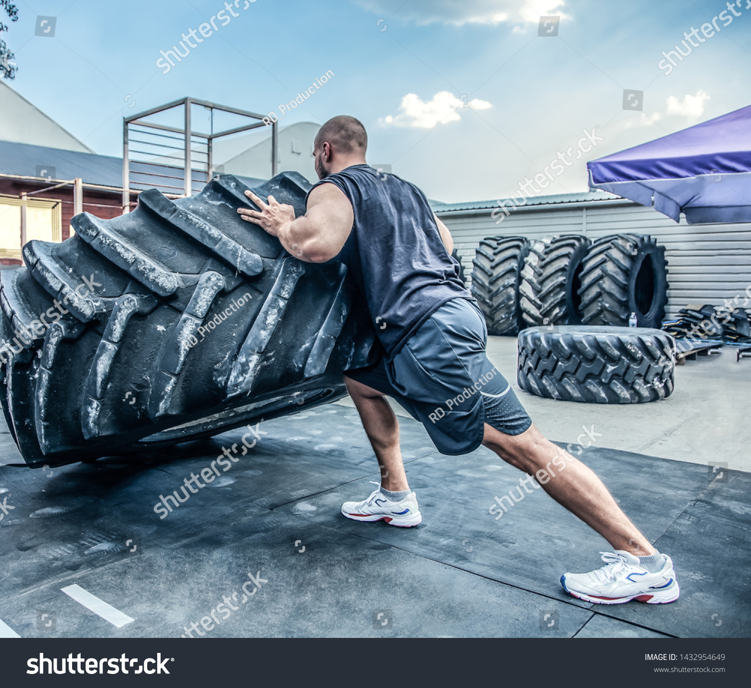 back view of strong muscular fitness man moving large tire in street gym. Concept lifting, workout training. #1432954649