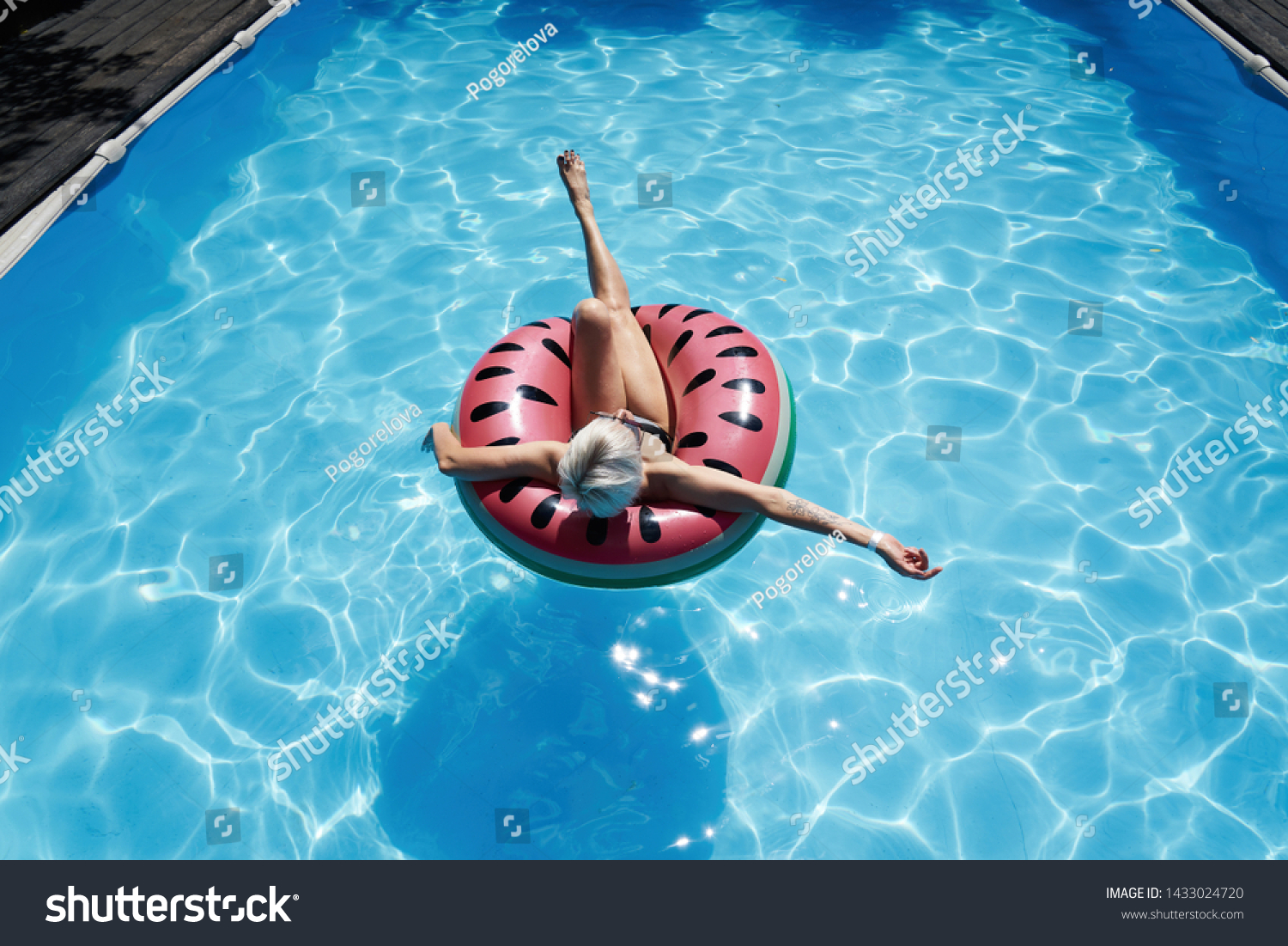 Woman with short hair swimming relaxing in a pool with pink floatie Inflatable doughnut, blue water, chill, tanning under sun.                        #1433024720