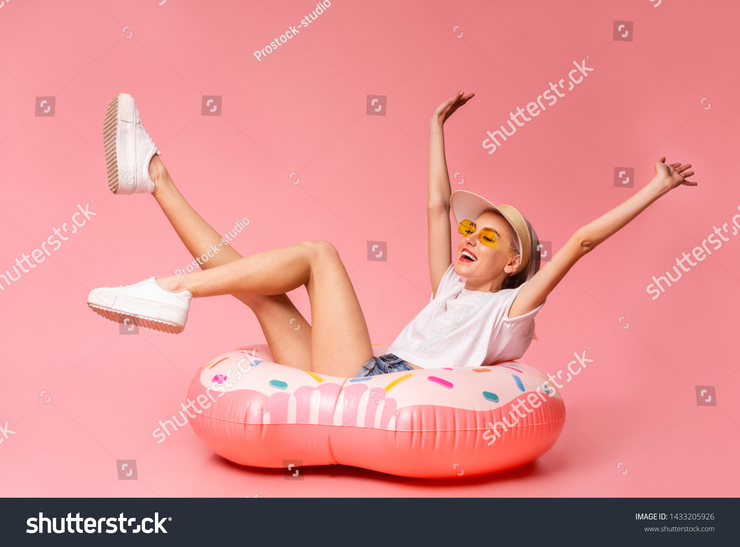 Positive millennial blonde sitting on big inflatable ring, ready to swim, pink studio background #1433205926