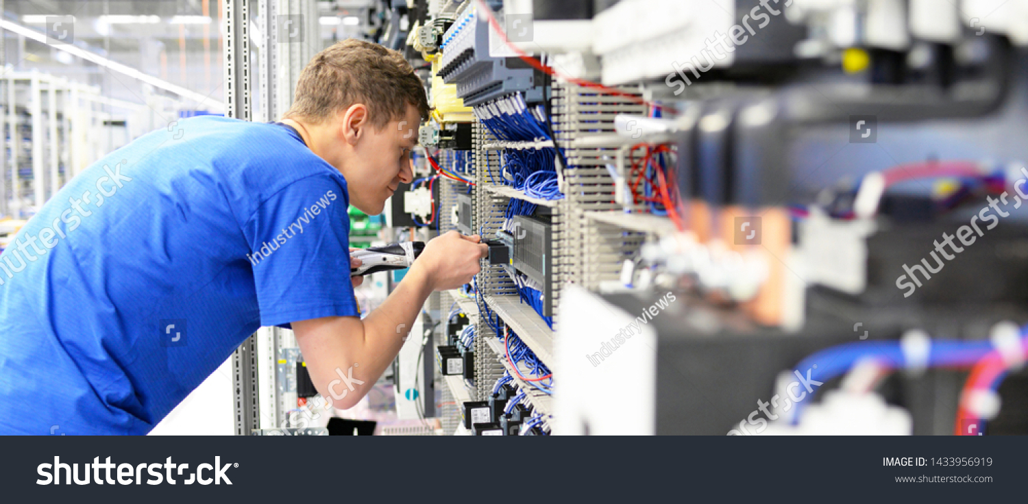 young apprentice worker in an industrial company assembling electronic components in the mechanical engineering of a modern factory  #1433956919